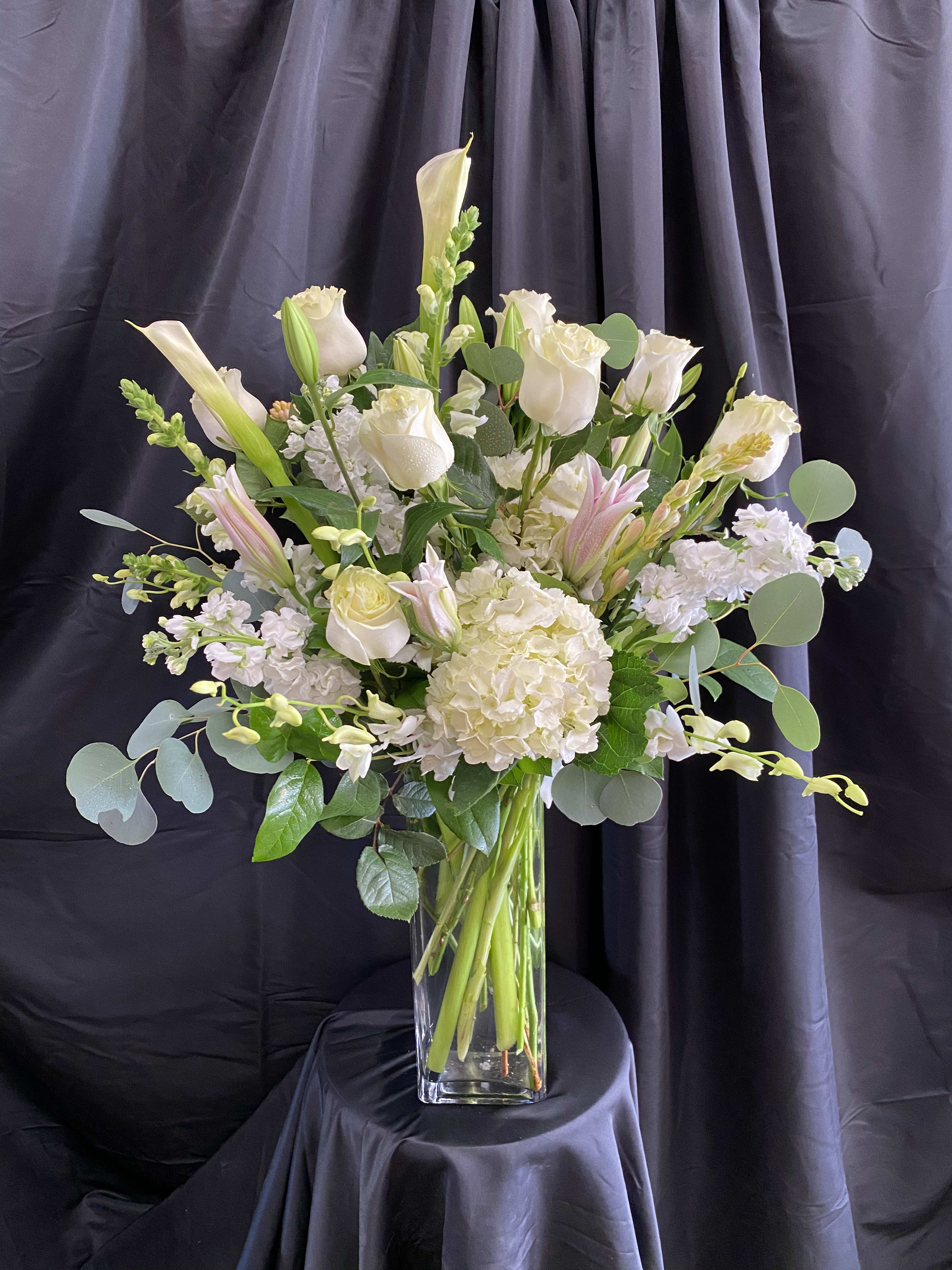 White roses and lilies arranged in a tall glass vase