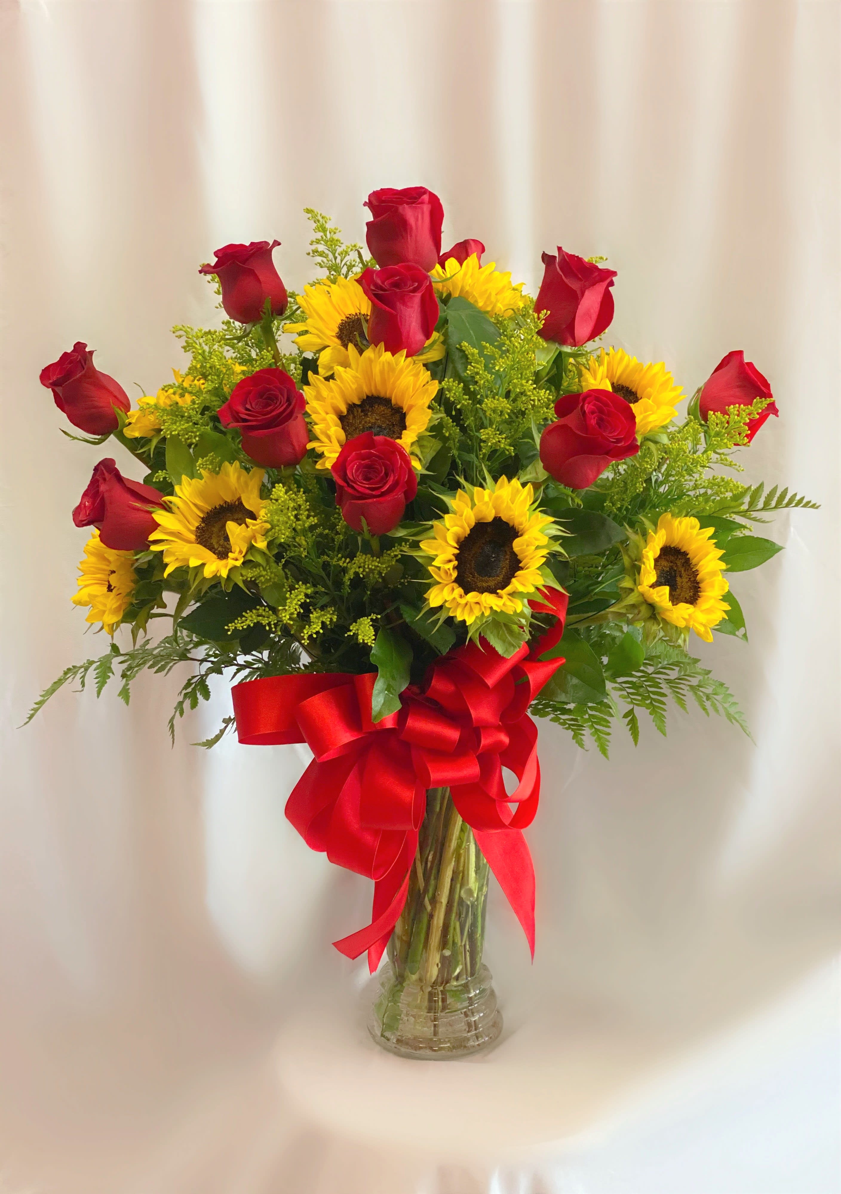 Bouquet of red roses and yellow sunflowers in a clear glass vase with a red ribbon