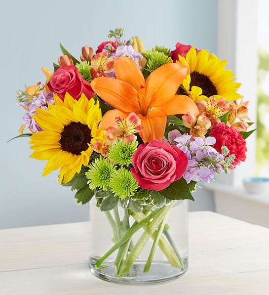 Mixed bouquet with sunflowers, orange lilies, and pink roses in a glass vase
