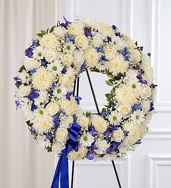 White floral wreath with blue accents on a black stand