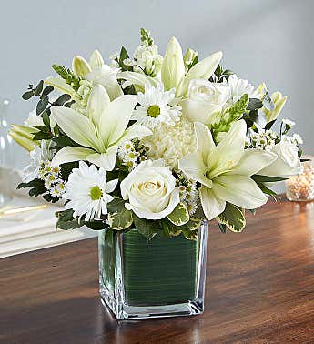 White lilies and roses arranged in a square glass vase