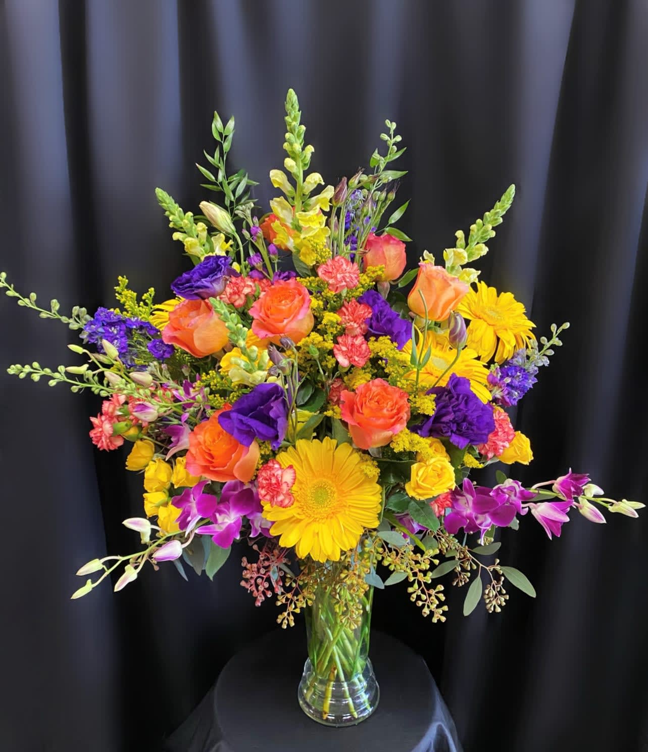 Bright mixed bouquet of roses, gerbera daisies, and orchids in a clear vase