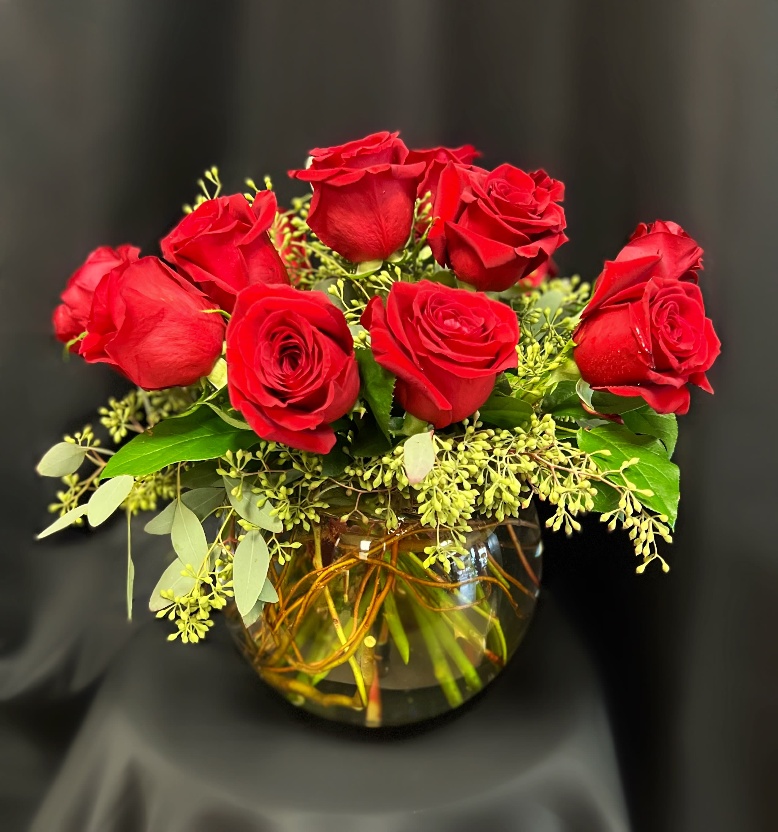 Red roses arranged in a round glass vase with greenery