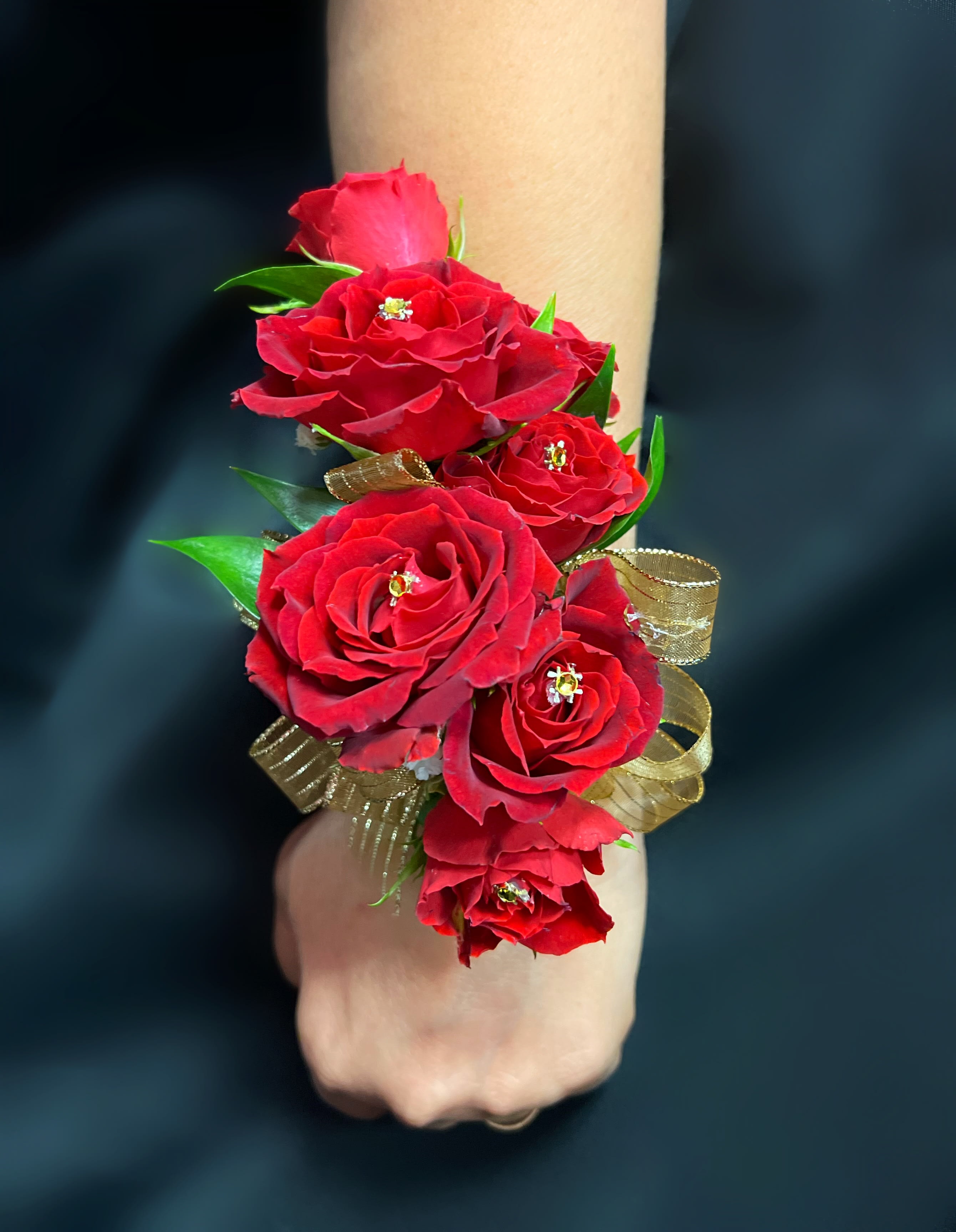 Red rose wrist corsage with gold ribbon on a wrist