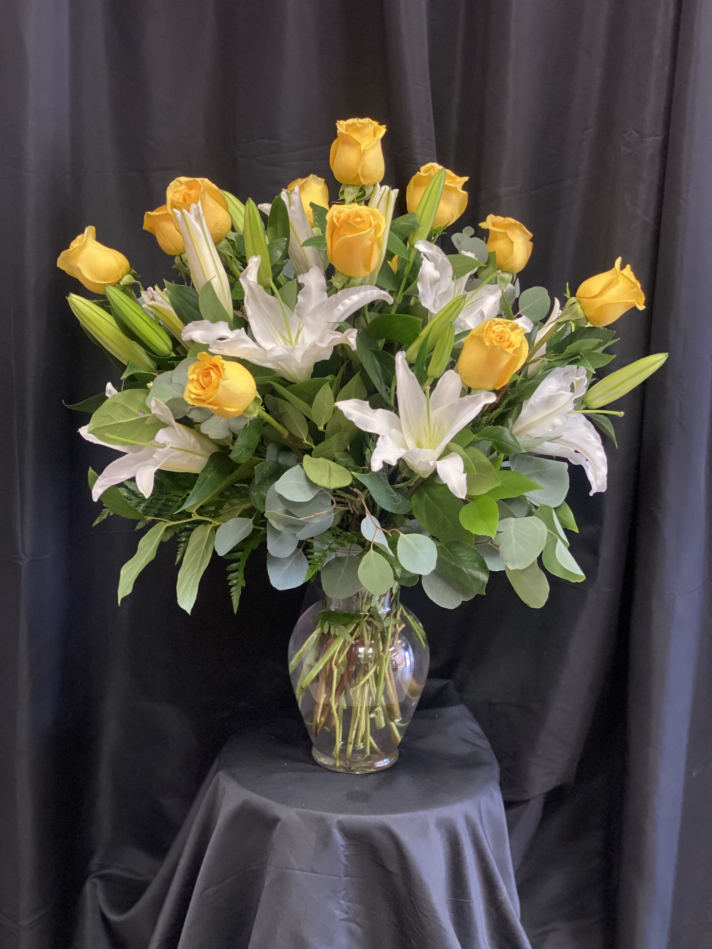 Yellow roses and white lilies arranged in a clear glass vase