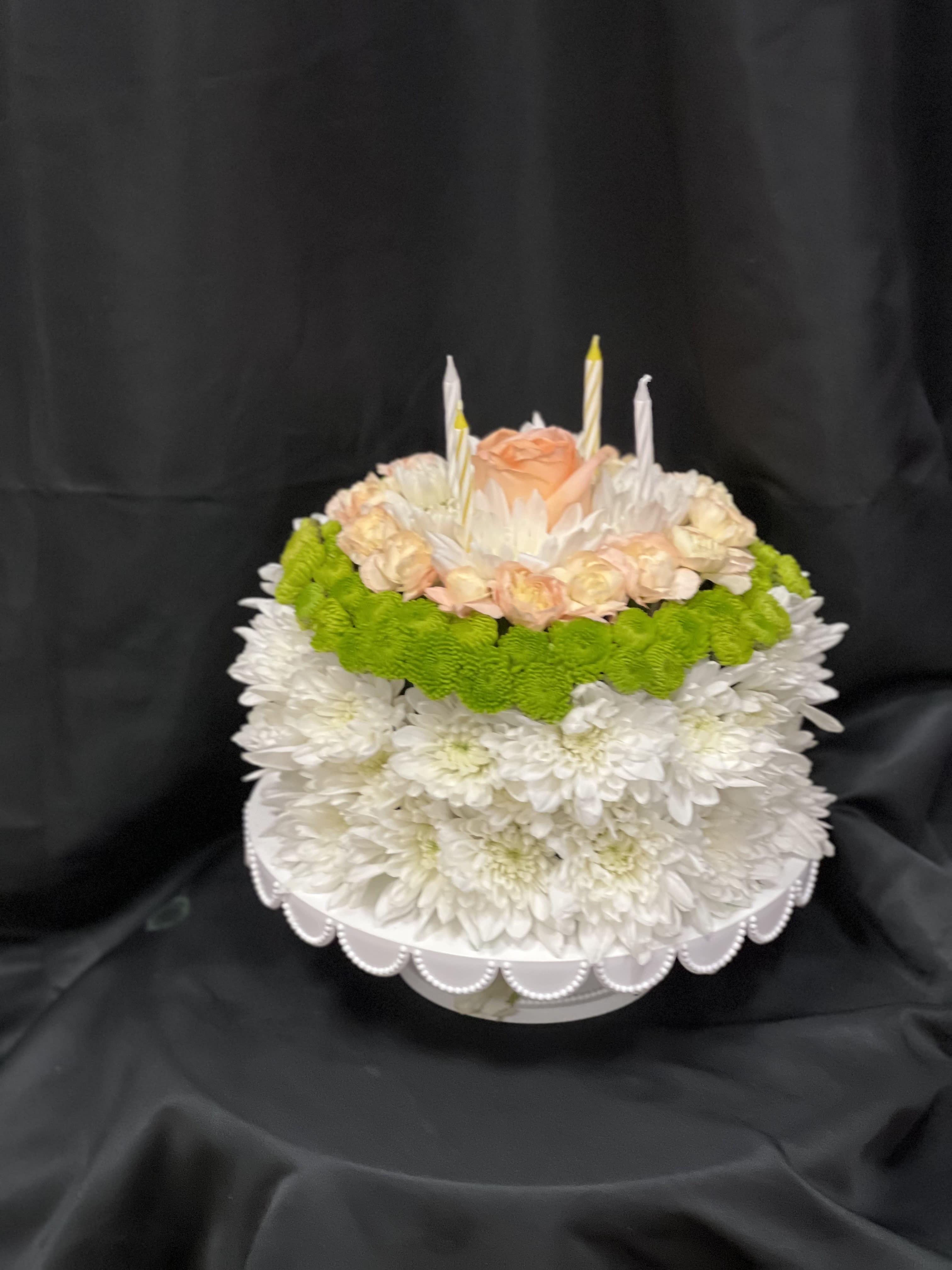 Round floral cake with white chrysanthemums, peach roses, and candles
