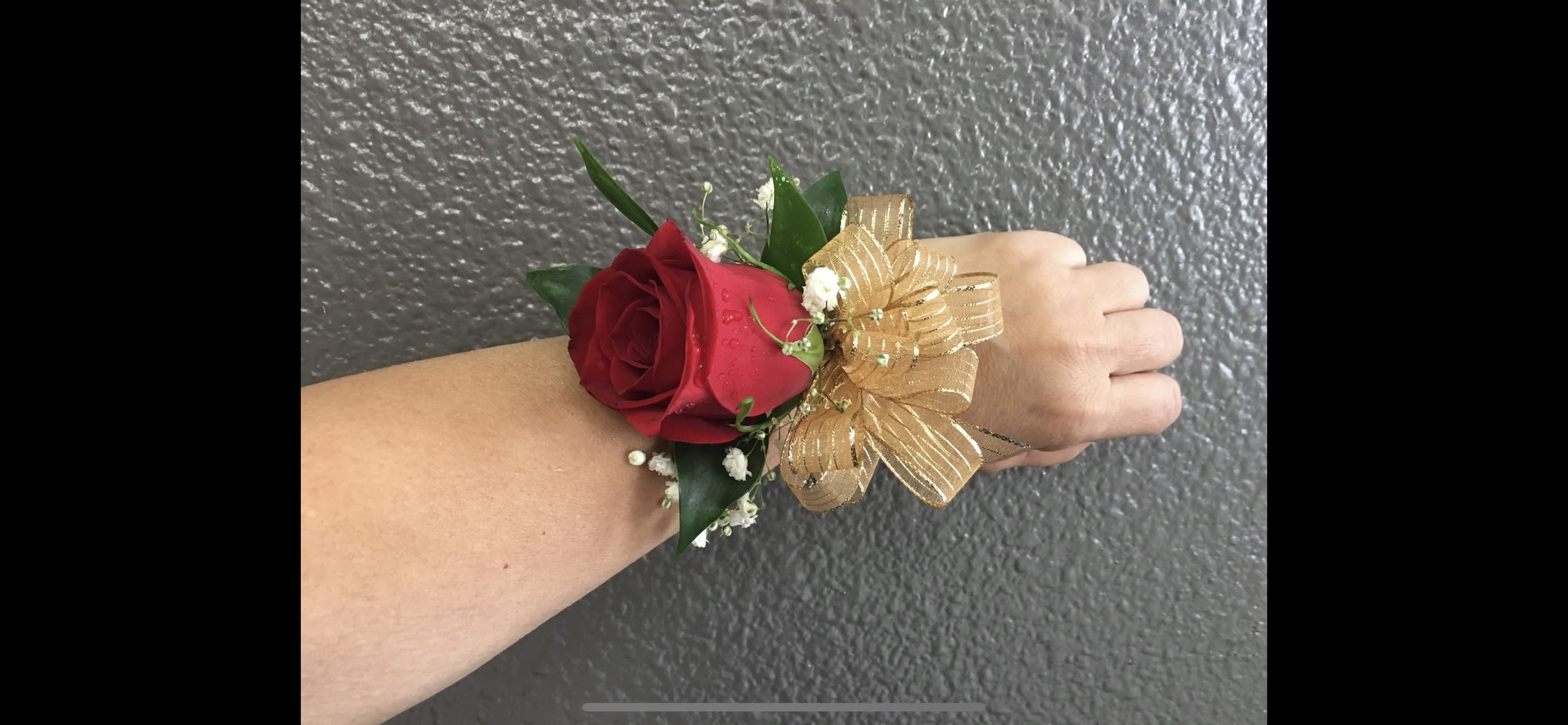Red rose wrist corsage with gold ribbon on an arm