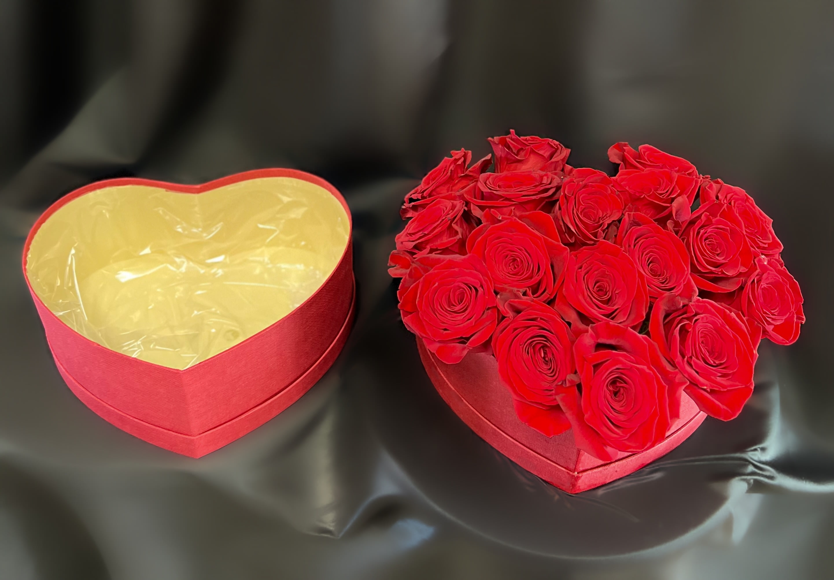 Heart-shaped box filled with red roses beside an empty matching box