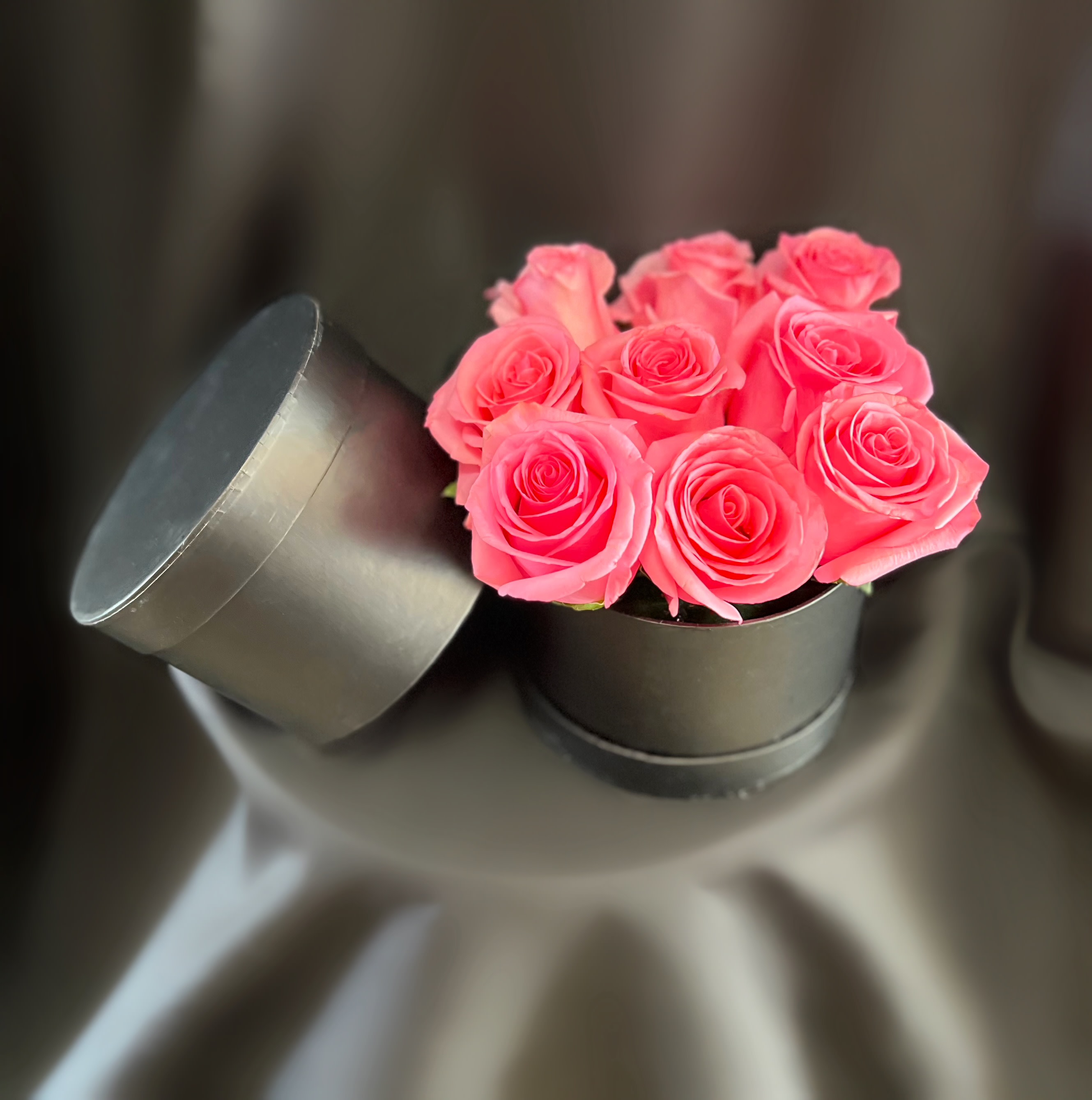 Pink roses in a black round box with the lid leaning beside it