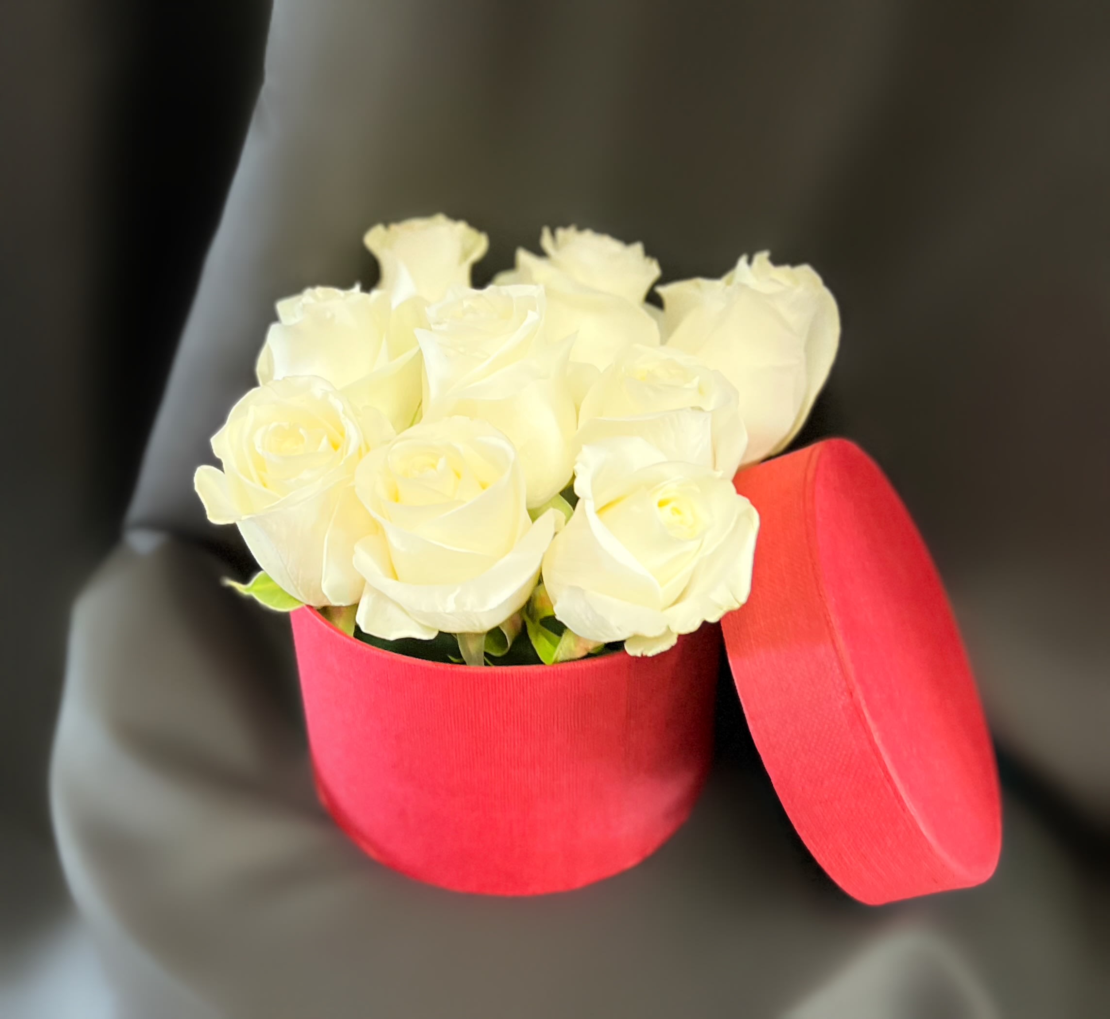 White roses in a red round box with the lid beside it