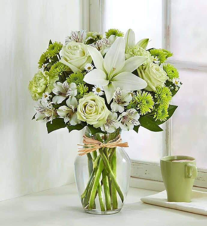 White lilies and roses in a clear glass vase with green mums