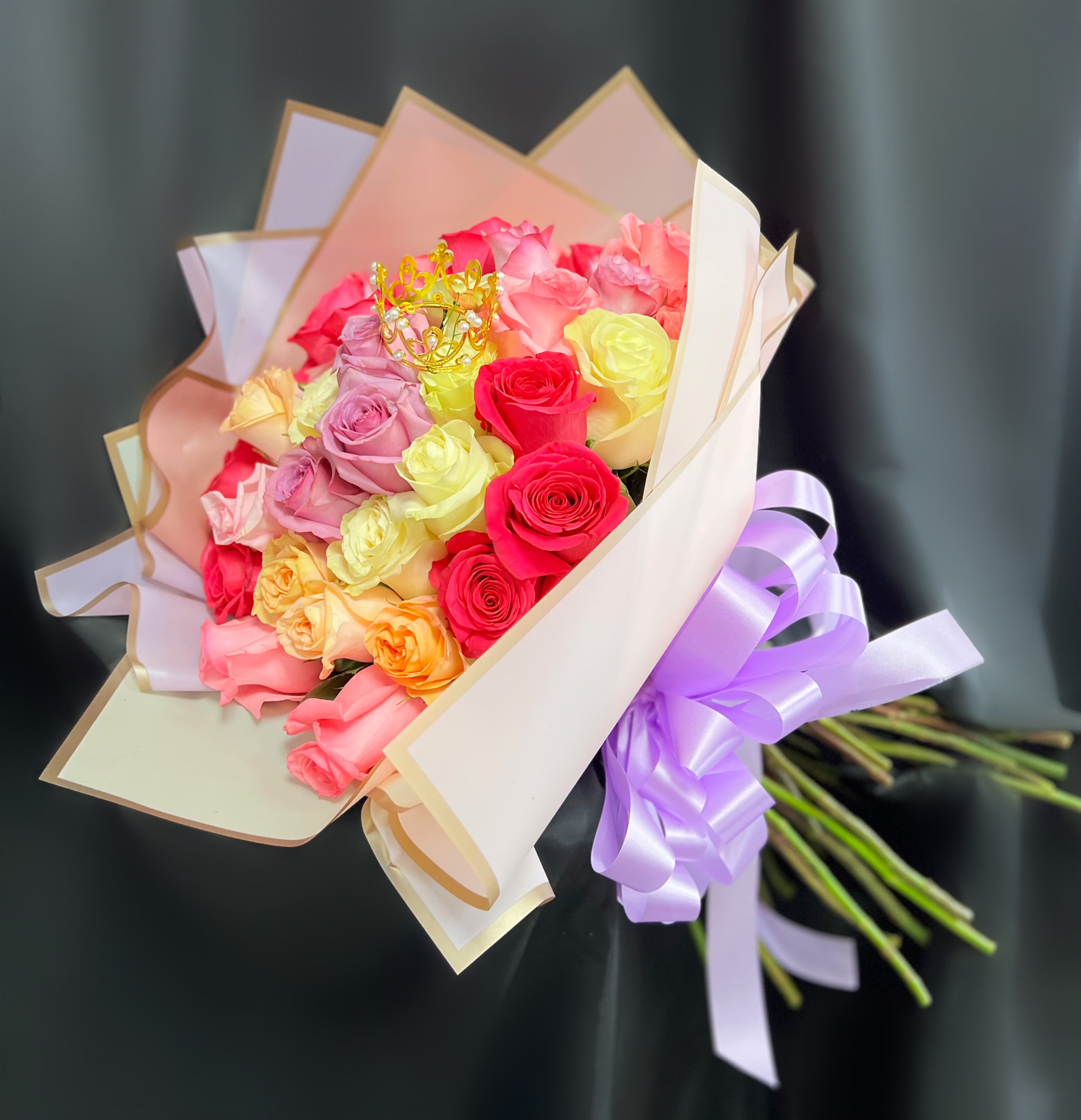 Bouquet of multicolored roses wrapped in pastel paper with a purple ribbon