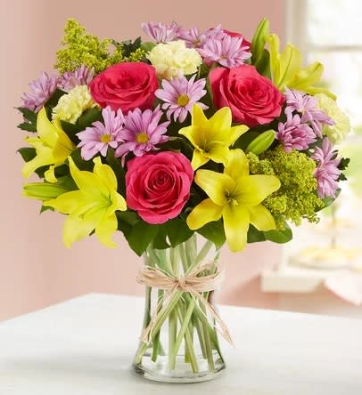 Bouquet of pink roses, yellow lilies, and purple daisies in a glass vase