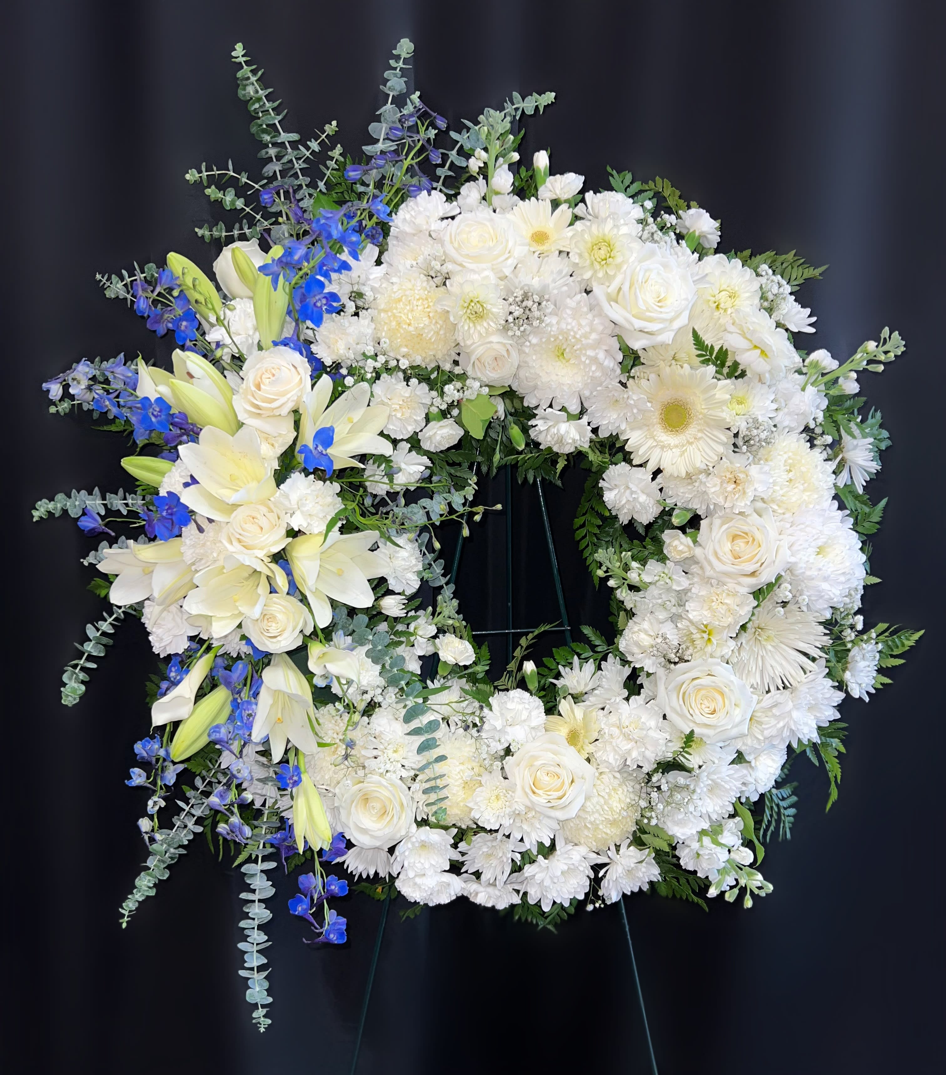 White floral wreath with blue accents on a stand