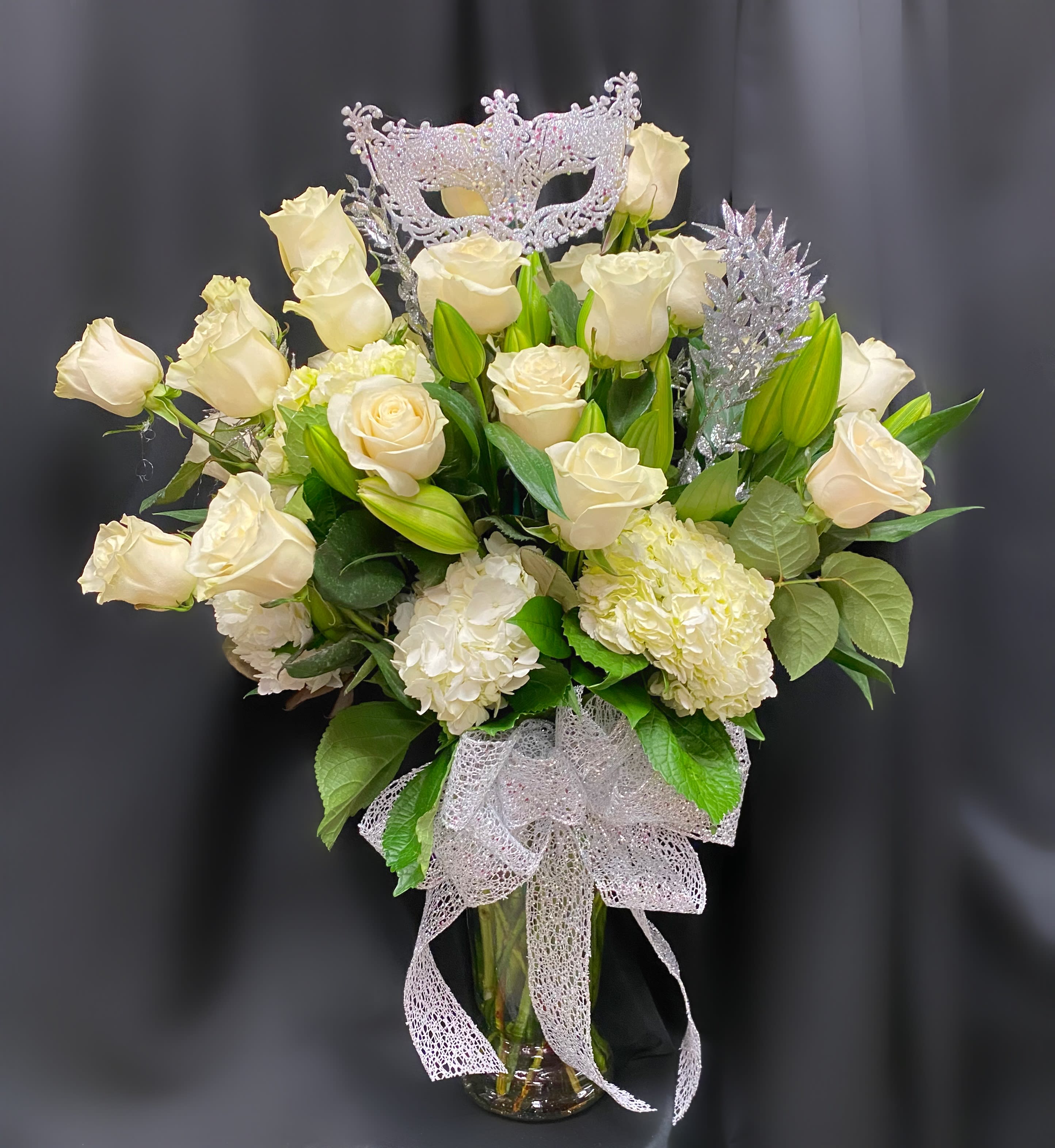Cream roses and white hydrangeas in a glass vase with a silver mask topper