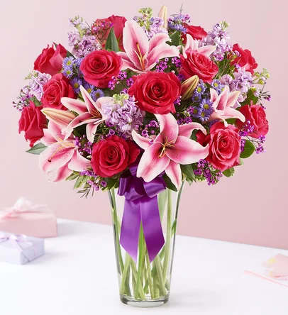 Bouquet of red roses and pink lilies in a clear glass vase with a purple ribbon