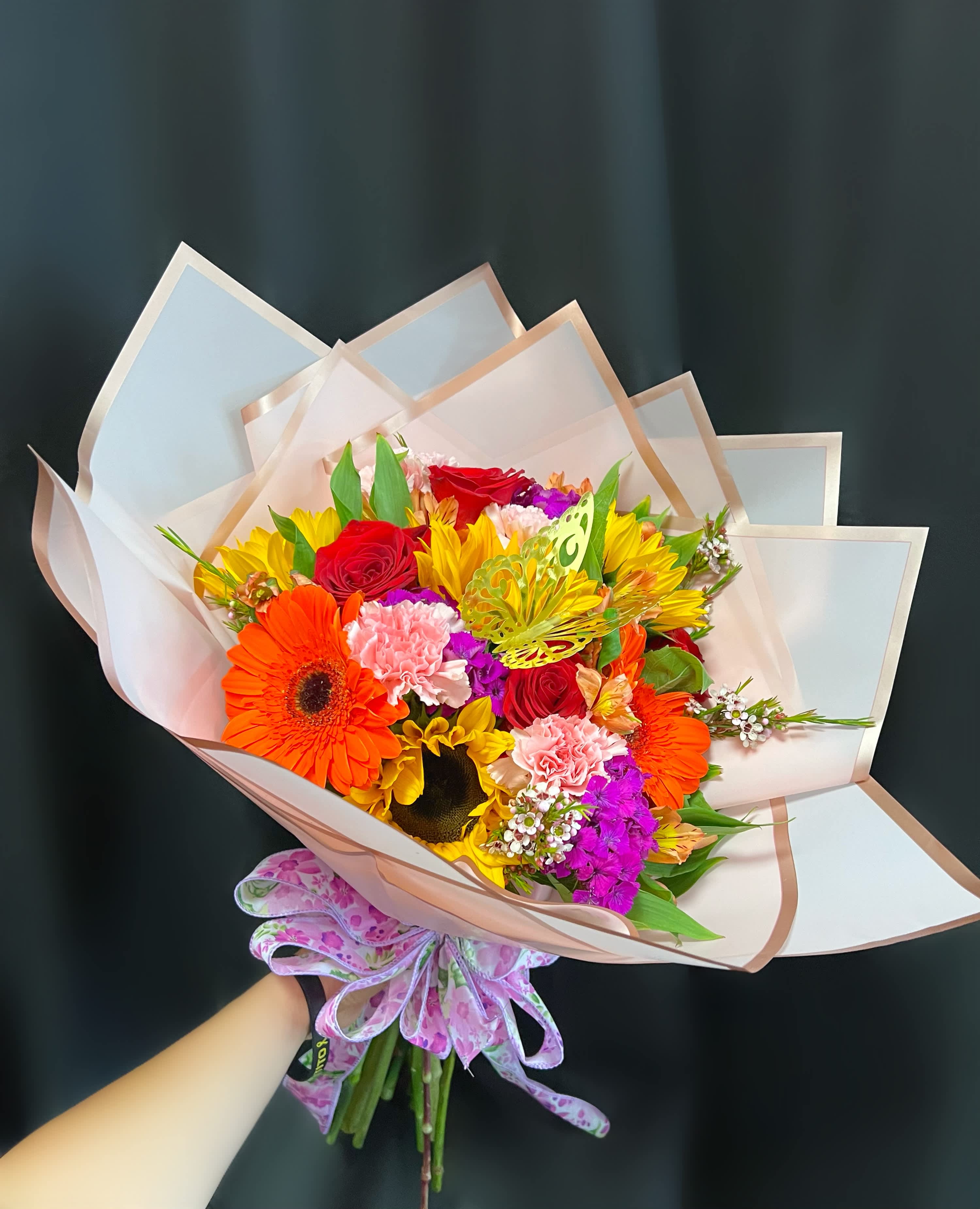 Colorful bouquet with roses, gerbera daisies, and carnations wrapped in pale paper