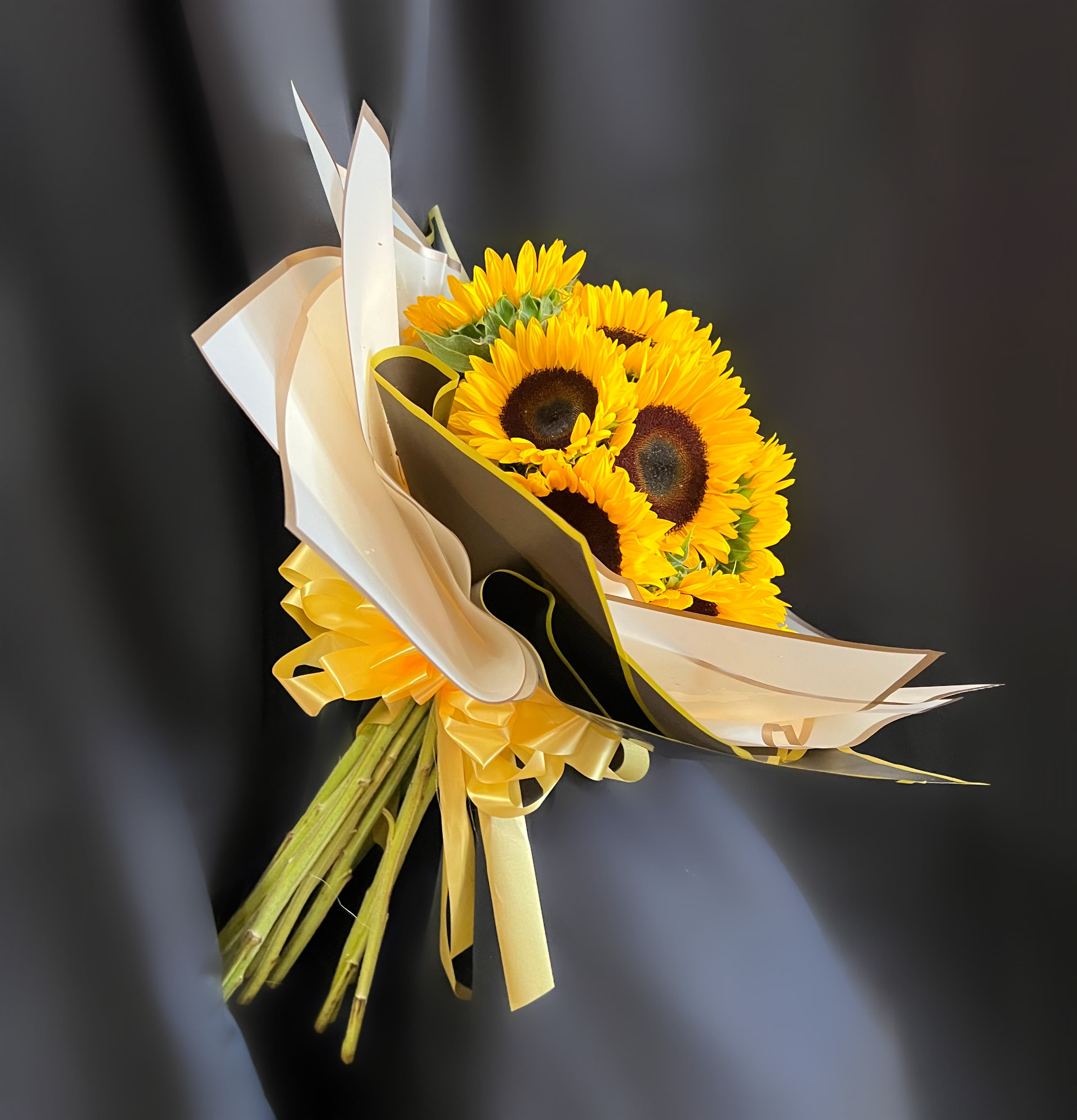 Bouquet of yellow sunflowers wrapped in cream and black paper with a yellow ribbon