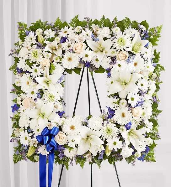 White floral wreath on a black easel with a blue ribbon bow