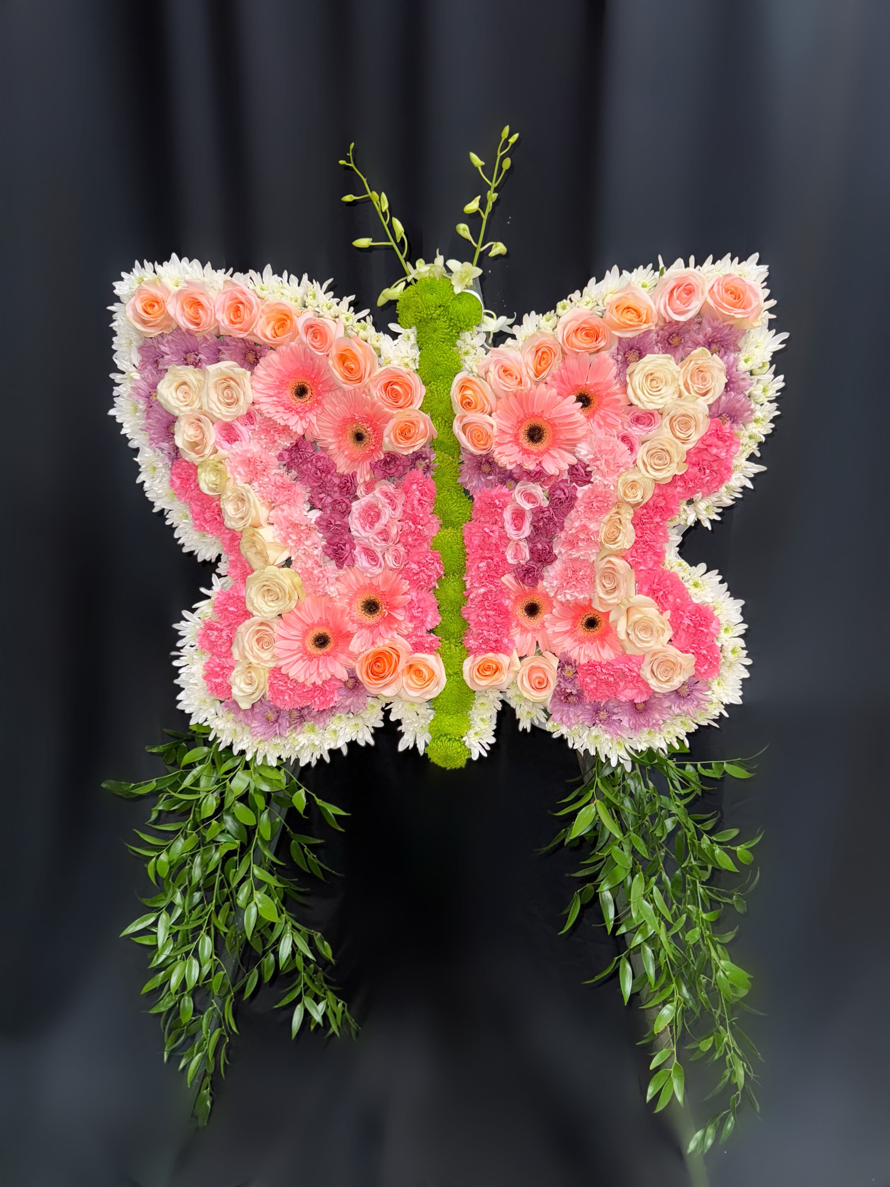 Butterfly-shaped floral arrangement with pink and peach blooms and trailing greenery