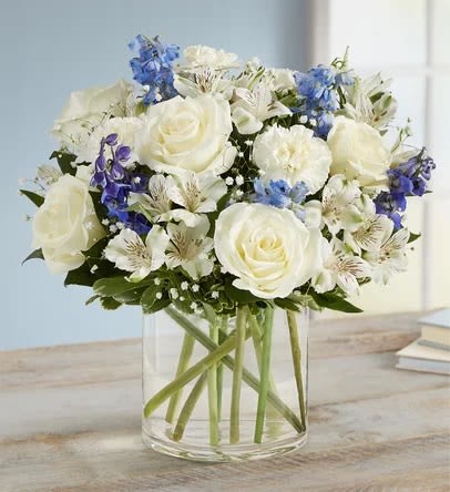 White roses and blue flowers in a clear glass vase