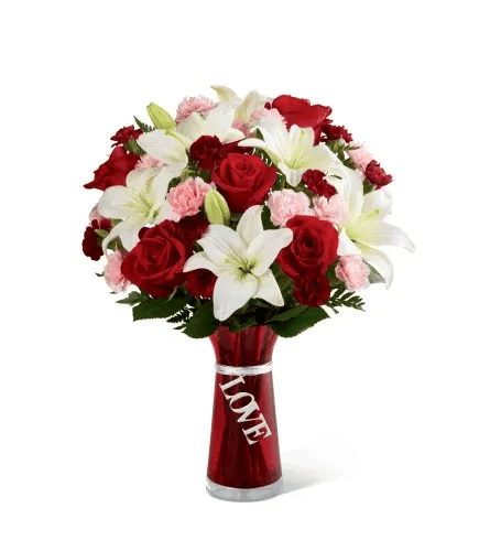 Red roses, white lilies, and pink carnations in a red vase with a LOVE ribbon