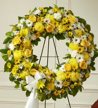 Yellow and white floral wreath on a black stand with a white ribbon