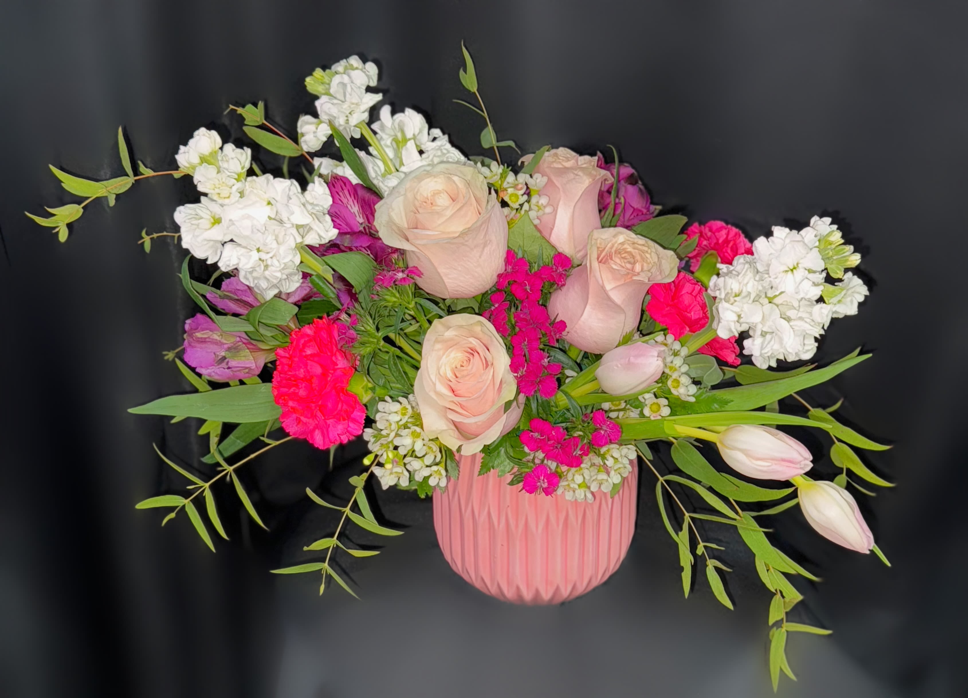Pink and white roses arranged in a pink vase with greenery