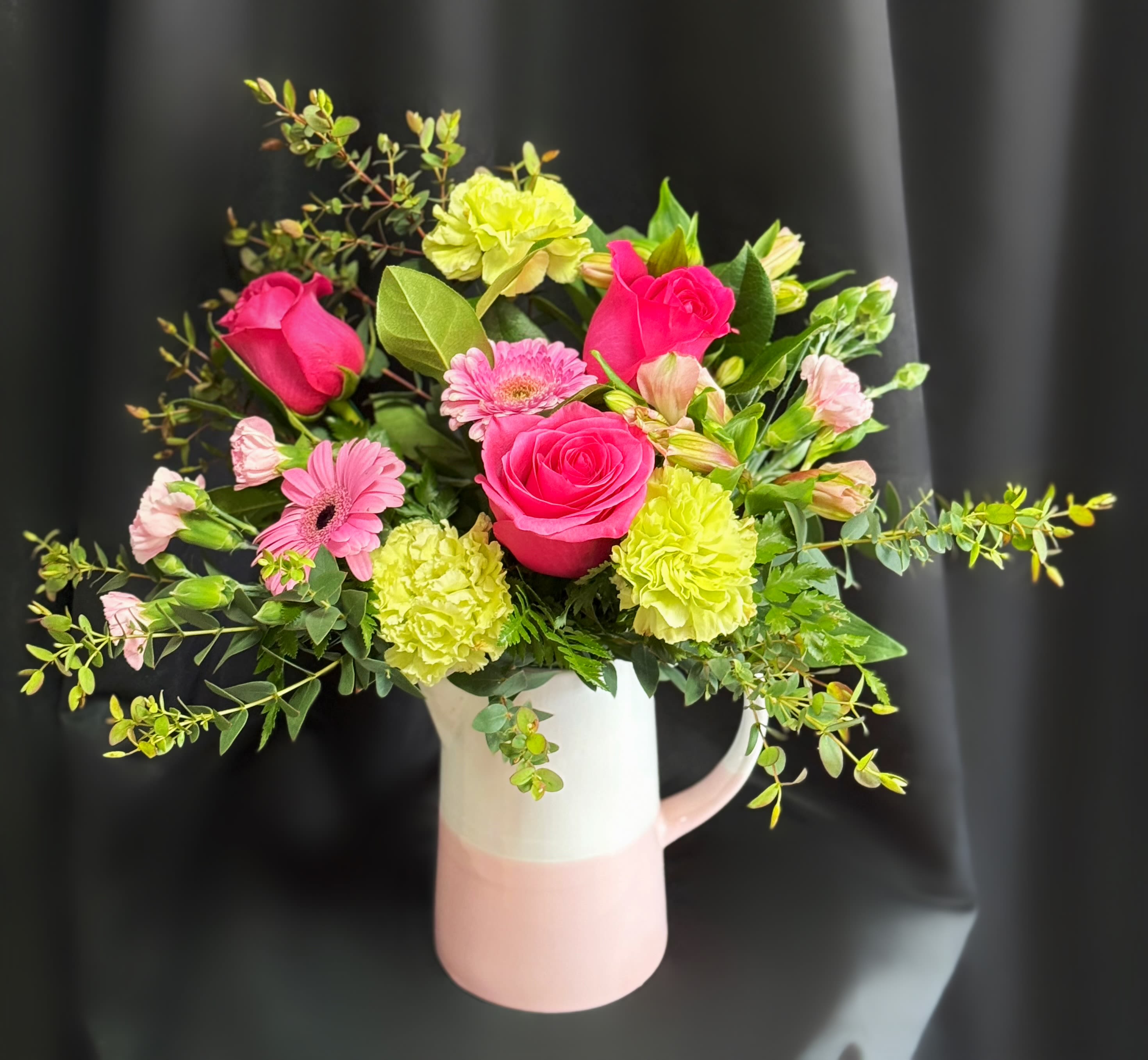 Pink roses and gerbera daisies in a white-and-pink pitcher vase