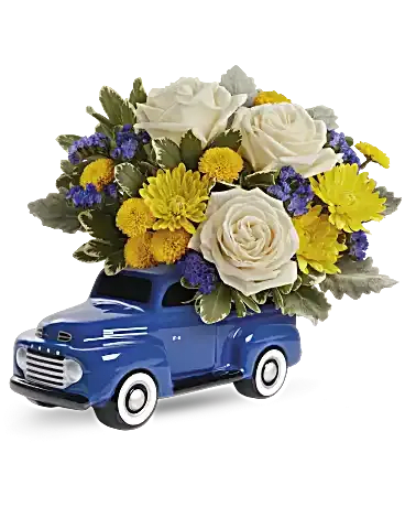 Blue toy truck topped with white roses and yellow flowers