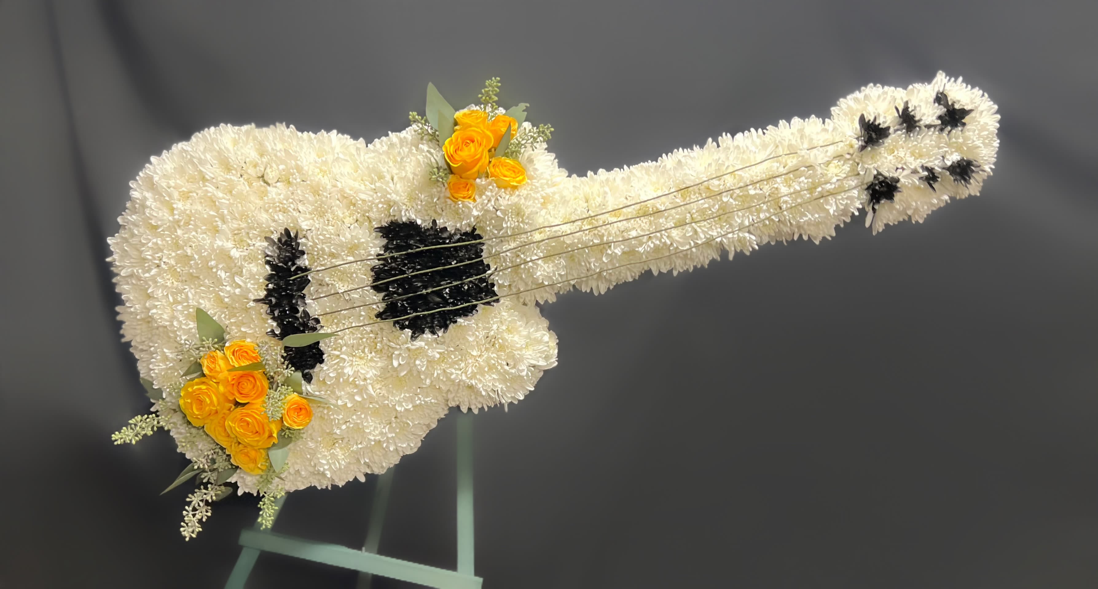 White floral guitar-shaped arrangement with yellow roses and black accents