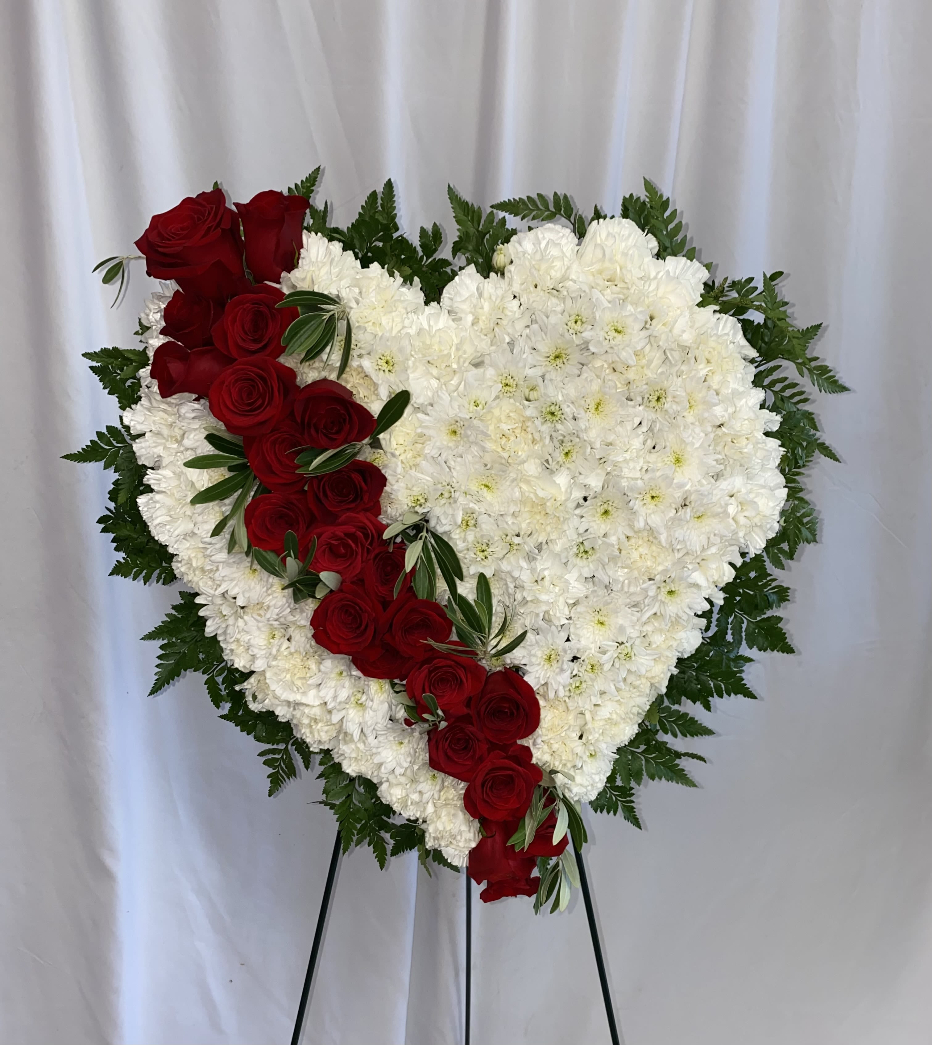 Heart-shaped floral tribute with red roses and white flowers on an easel