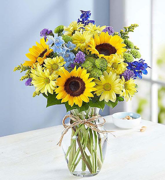 Bouquet of sunflowers, yellow daisies, and blue flowers in a glass vase
