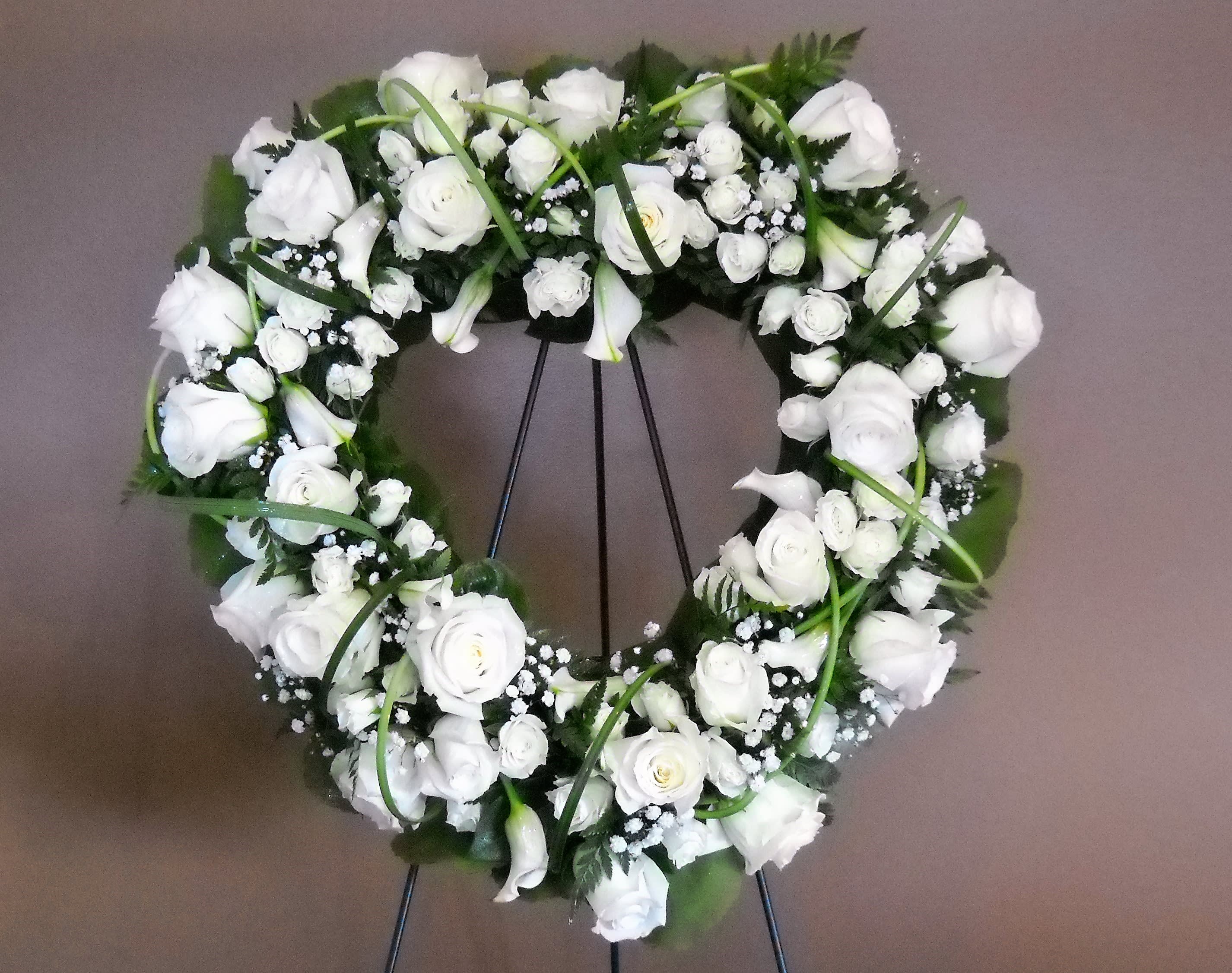 White floral wreath on a stand with roses and calla lilies