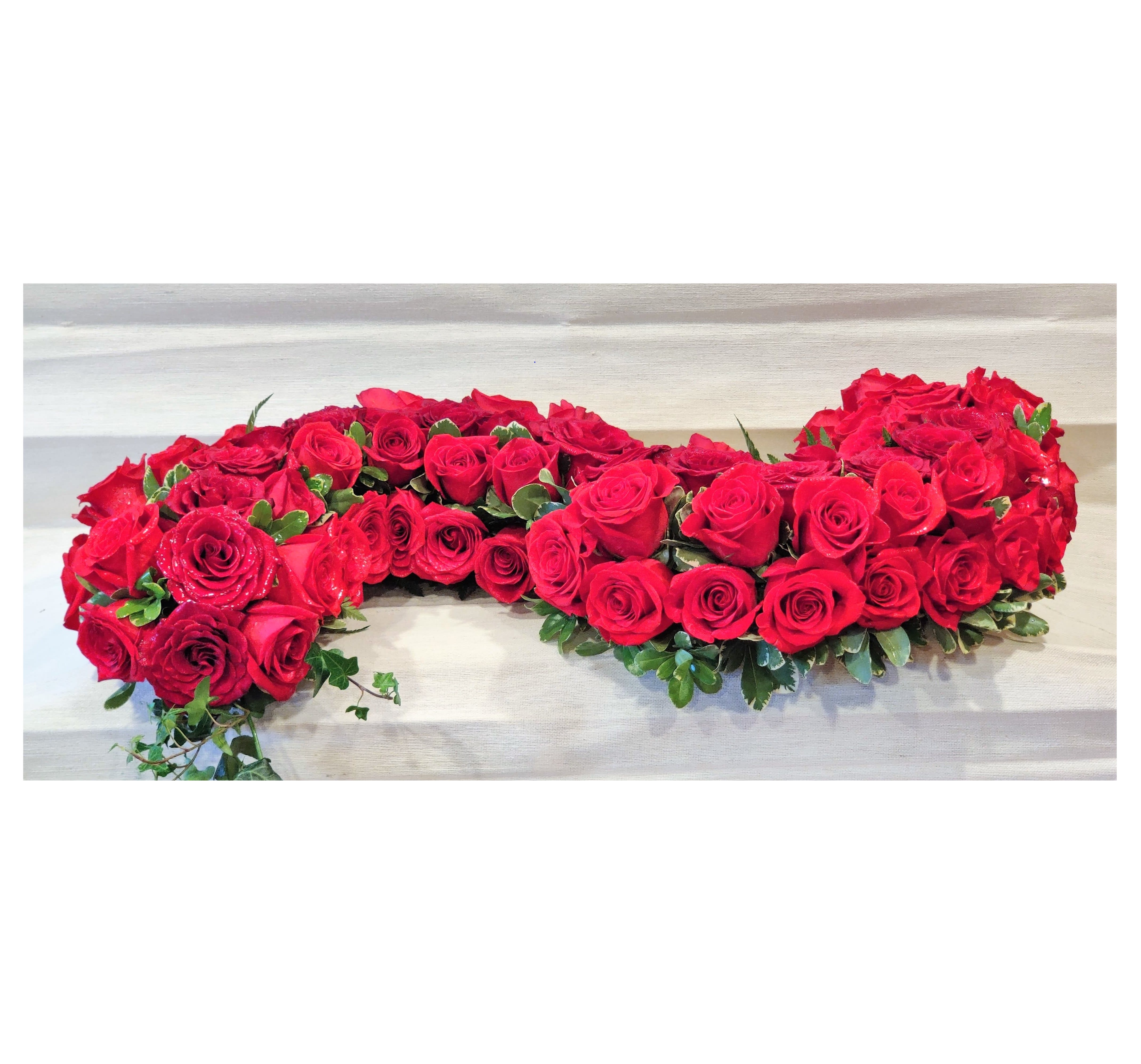 Heart-shaped arrangement of red roses with greenery
