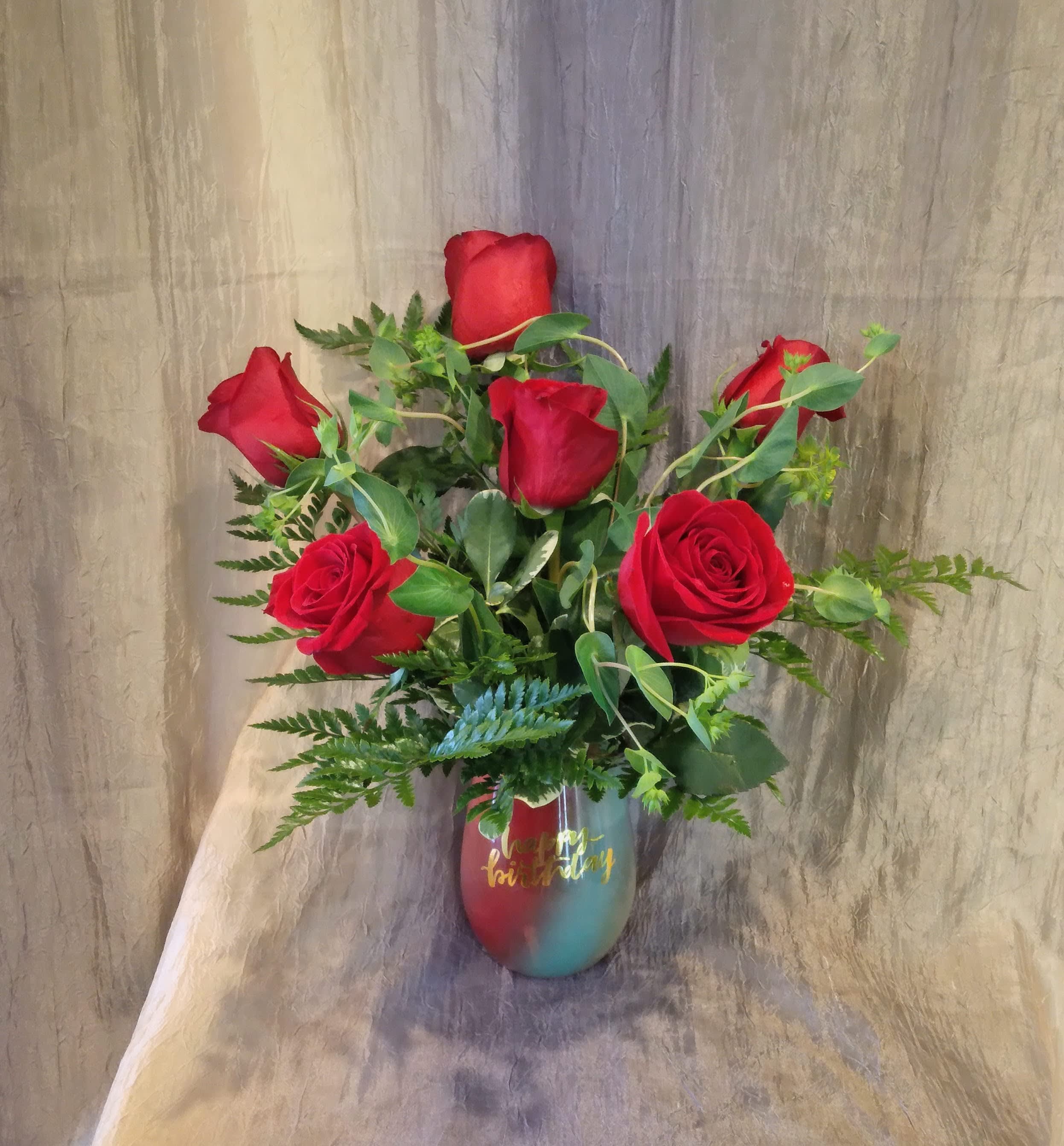 Red roses arranged in a multicolor vase with greenery