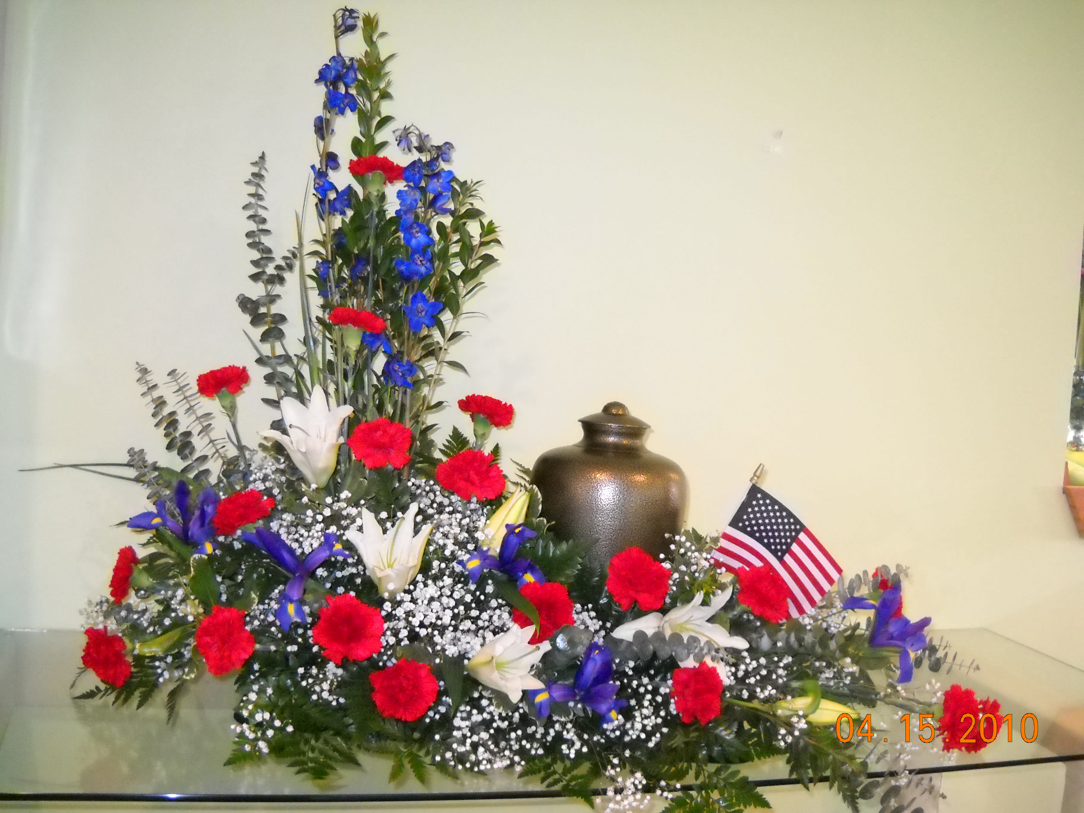 Red carnations and blue flowers arranged with white lilies and an American flag