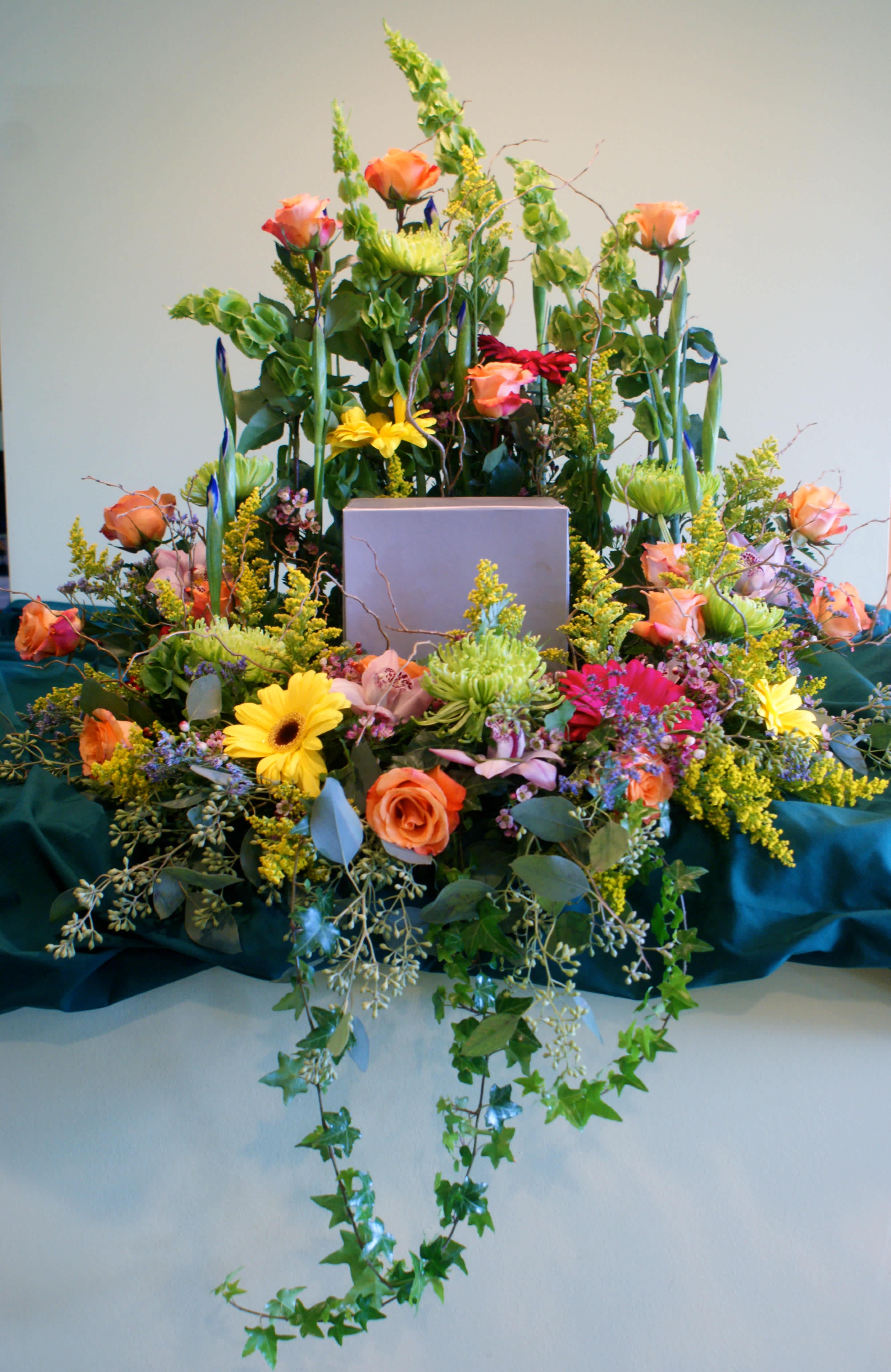 Large floral arrangement with roses, daisies, and tall greenery around a box