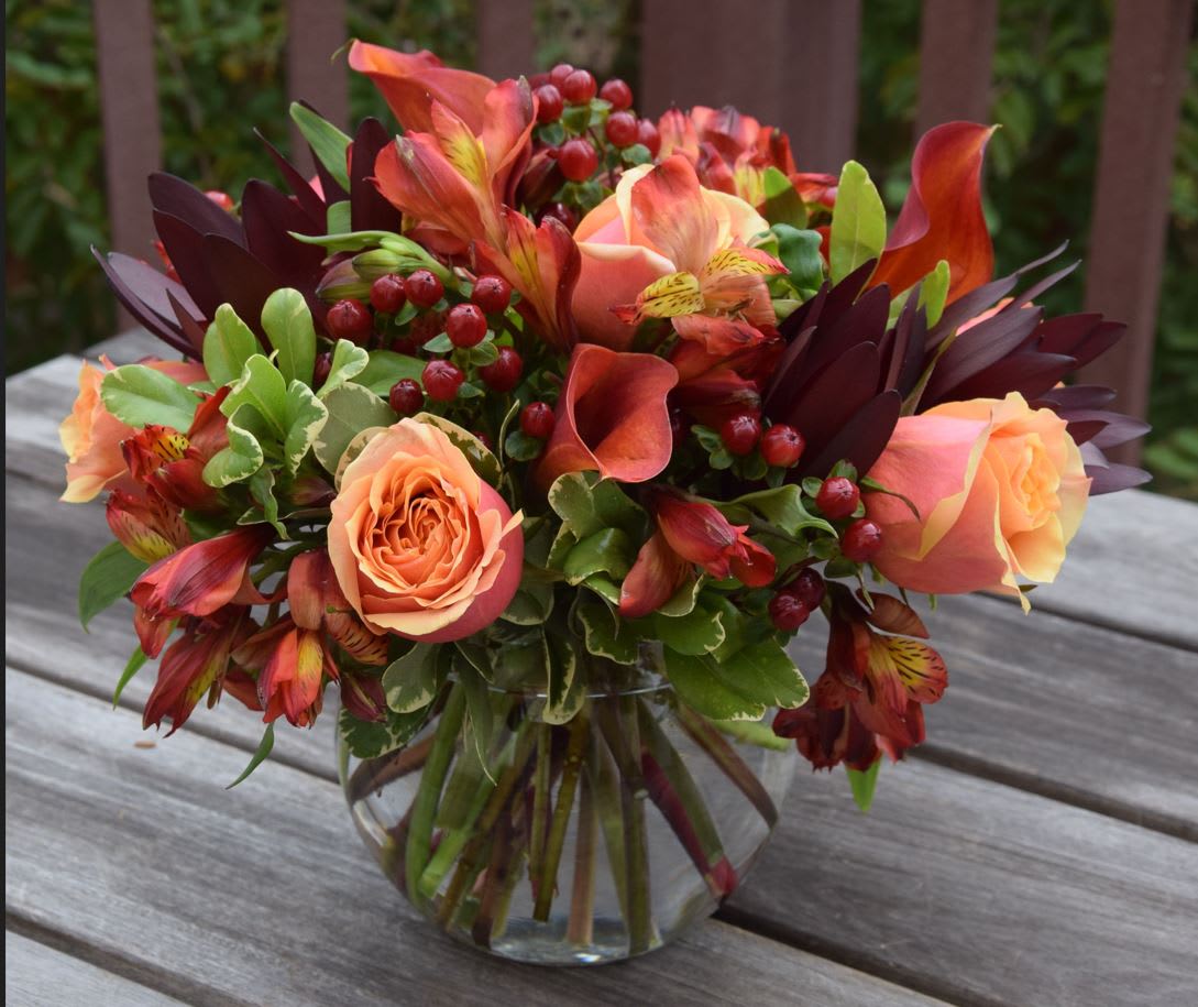 Peach roses and red-orange flowers arranged in a clear glass vase