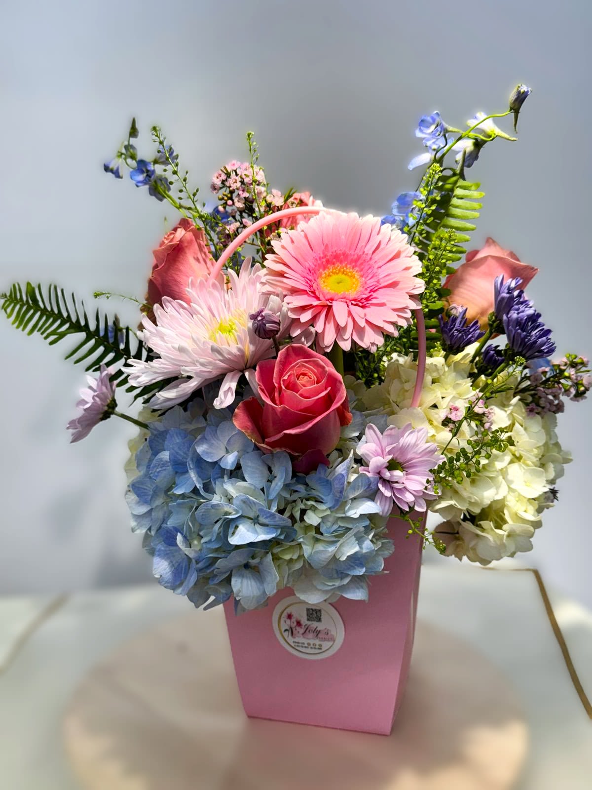 Pink and blue mixed flower arrangement in a pink box with a handle