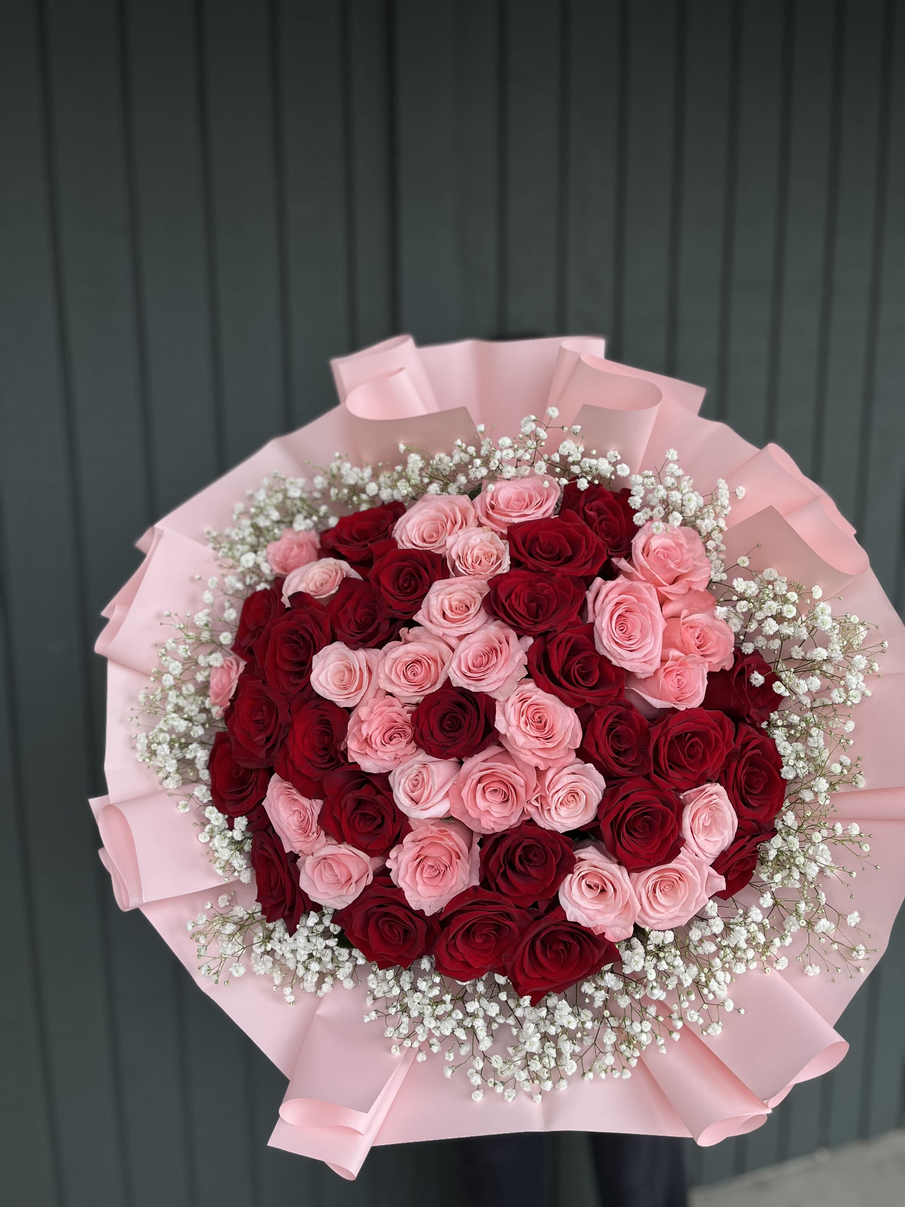 Bouquet of red and pink roses wrapped in pink paper with baby's breath