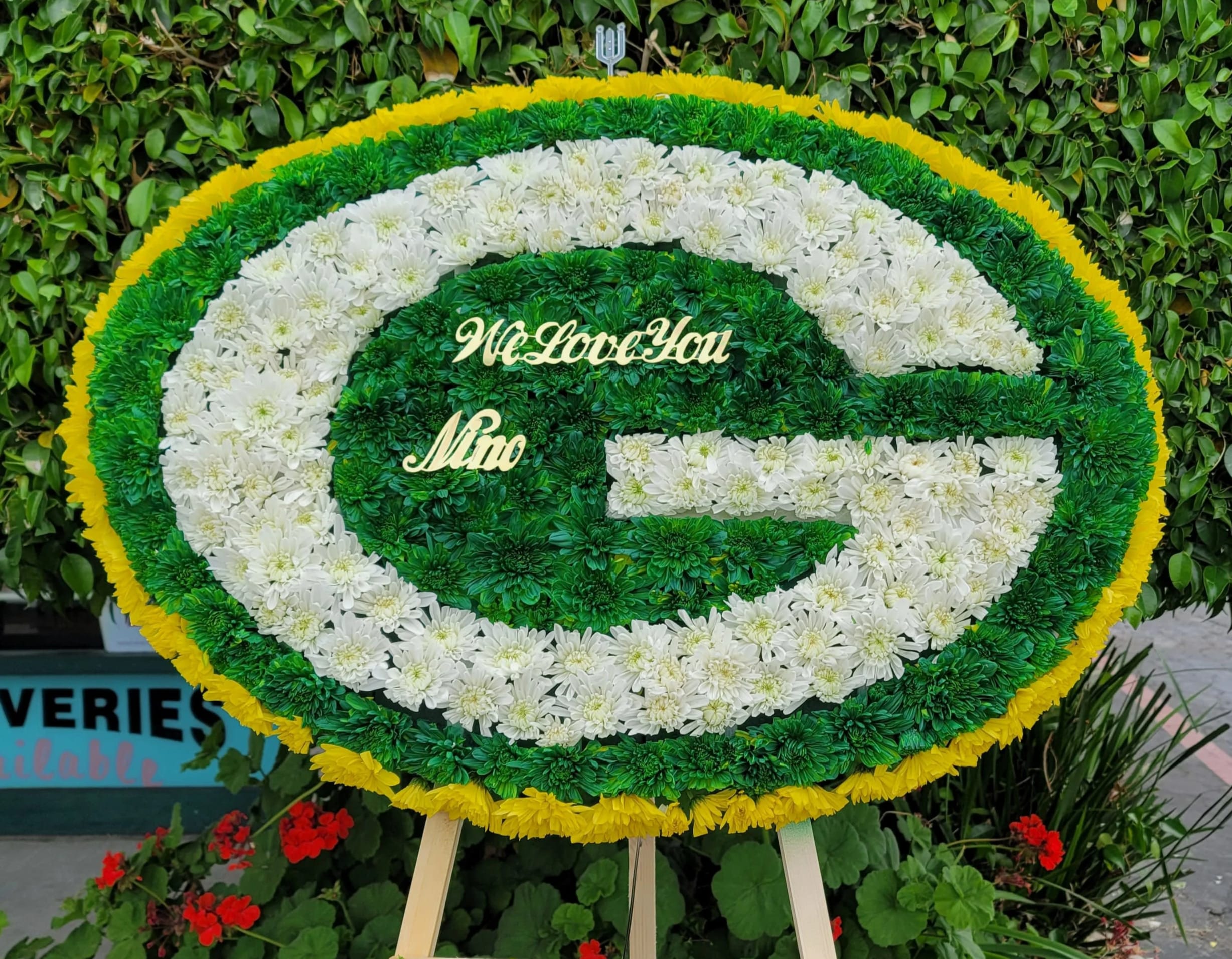 Oval floral tribute in green, white, and yellow with a message in the center