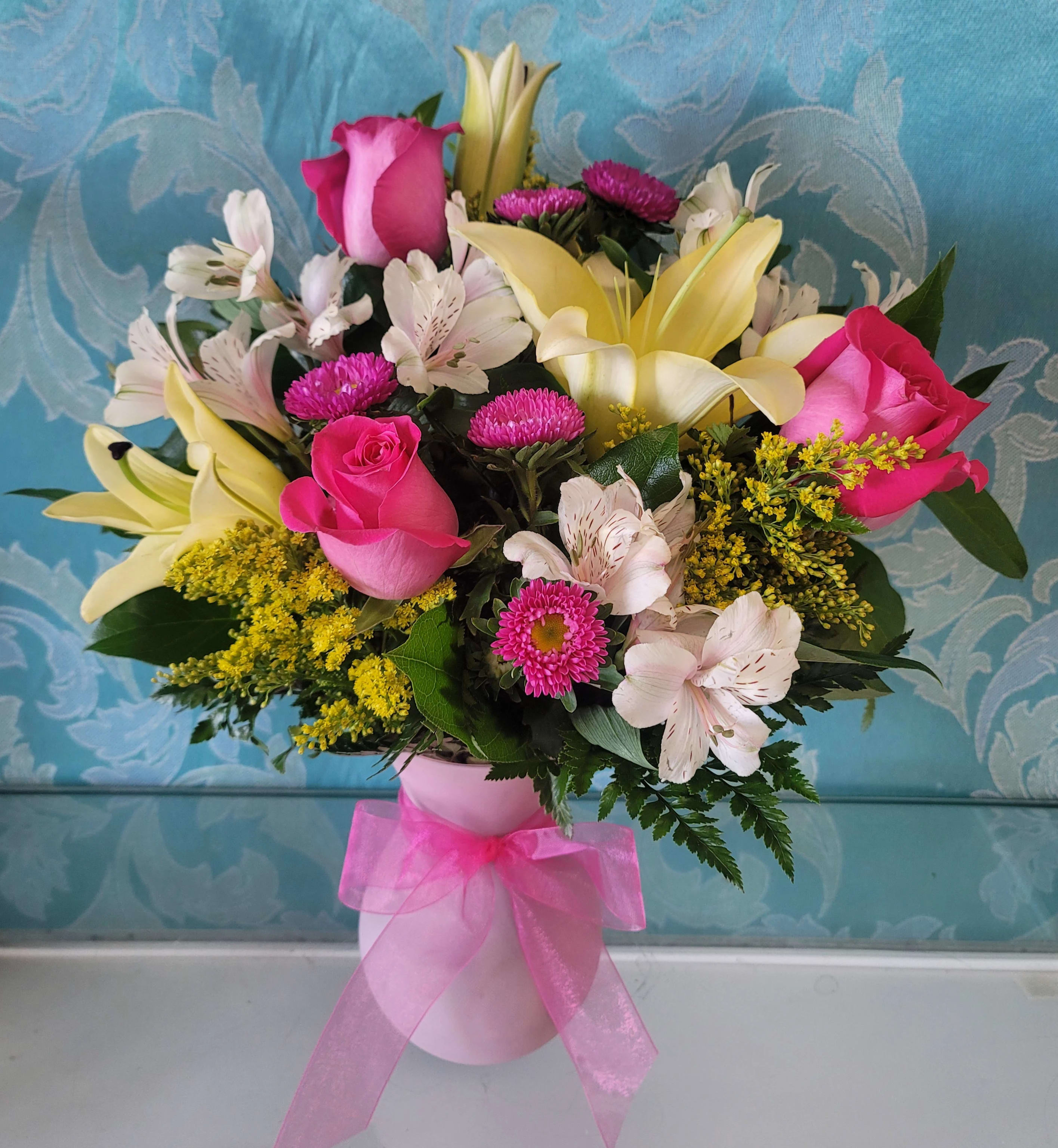 Bouquet of pink roses, lilies, and mixed flowers in a pink vase with ribbon