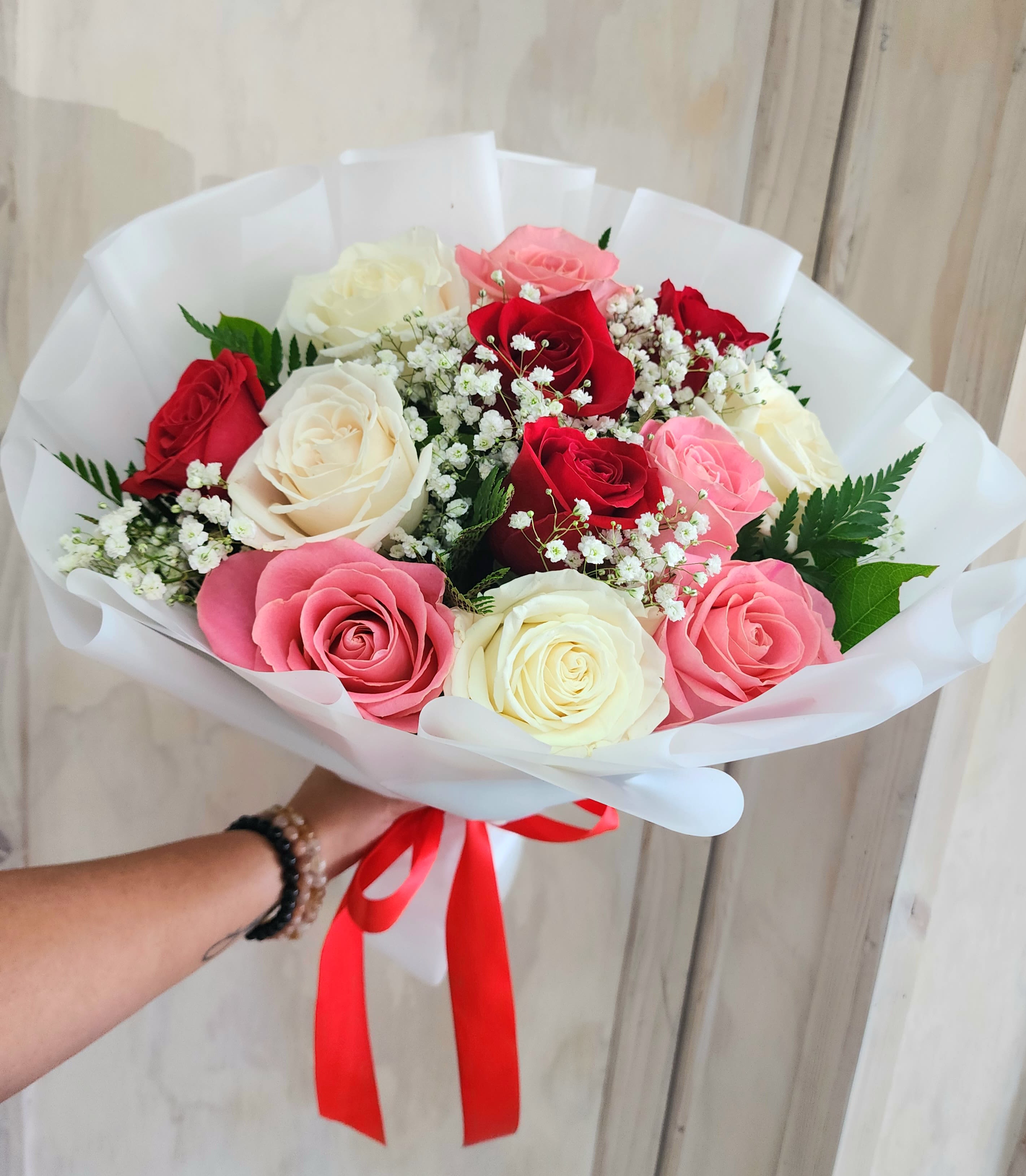 Handheld bouquet of red, pink, and white roses with baby's breath