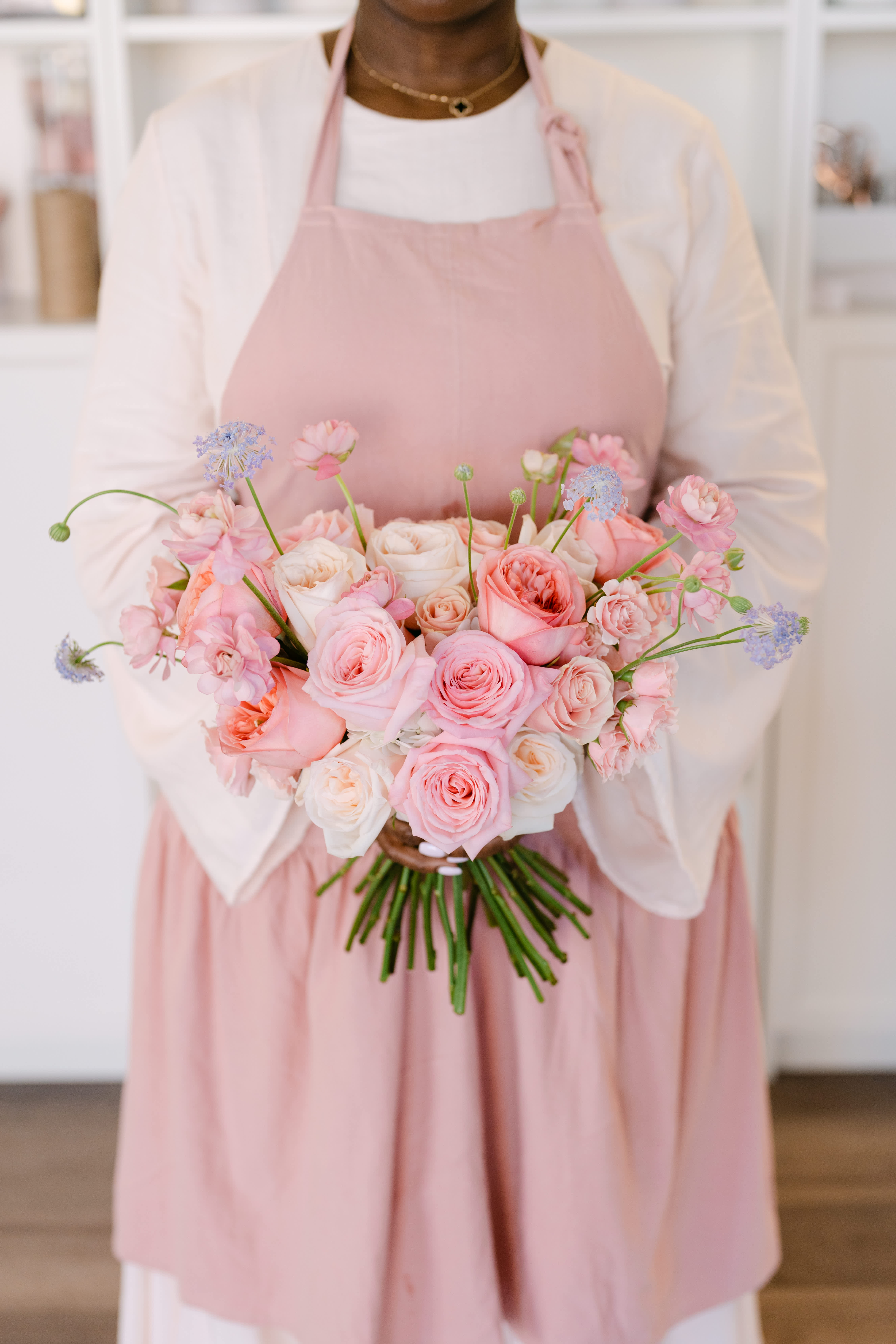 Person holding a bouquet of pink and white roses with small blue flowers