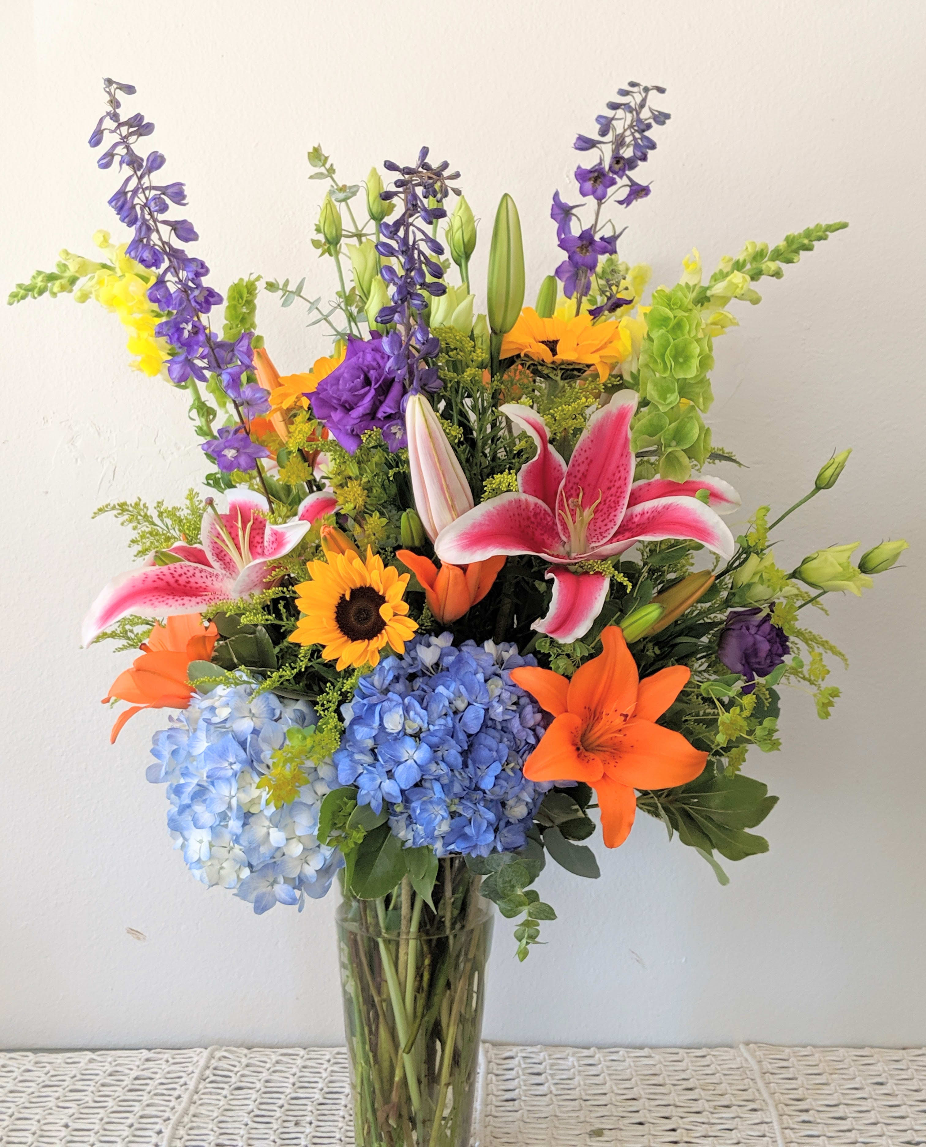 Colorful mixed bouquet in a clear glass vase with lilies, hydrangeas, and sunflowers