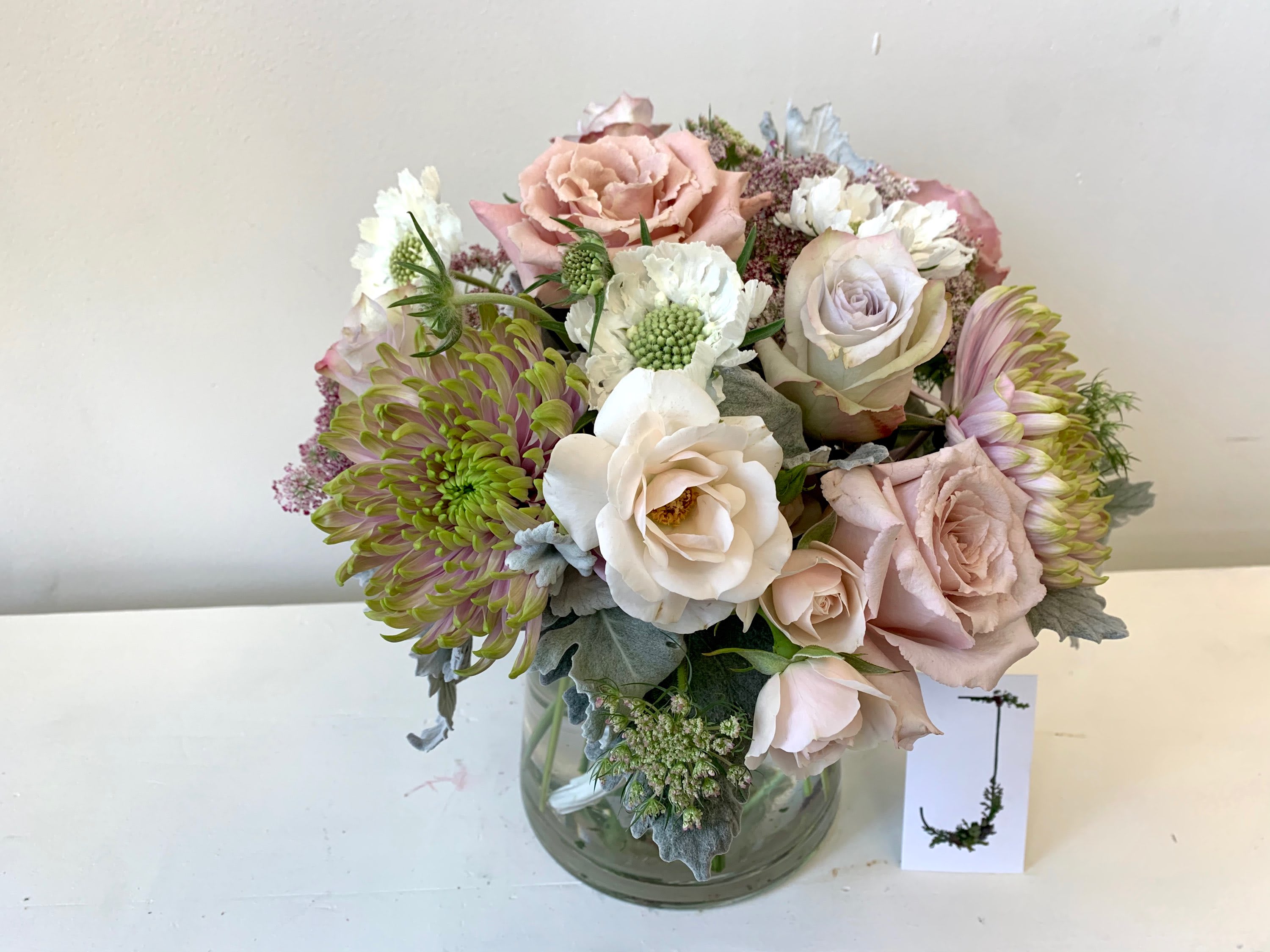 Pastel bouquet of roses, chrysanthemums, and white blooms in a glass vase