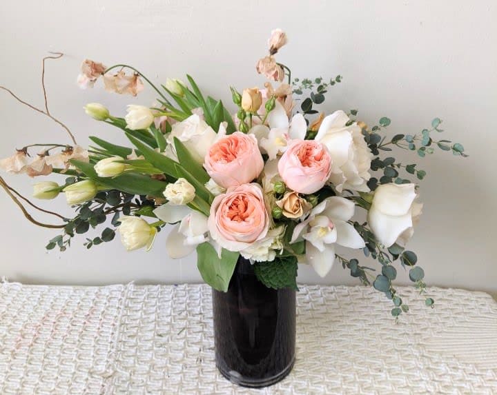 Bouquet of blush roses and white orchids in a dark vase