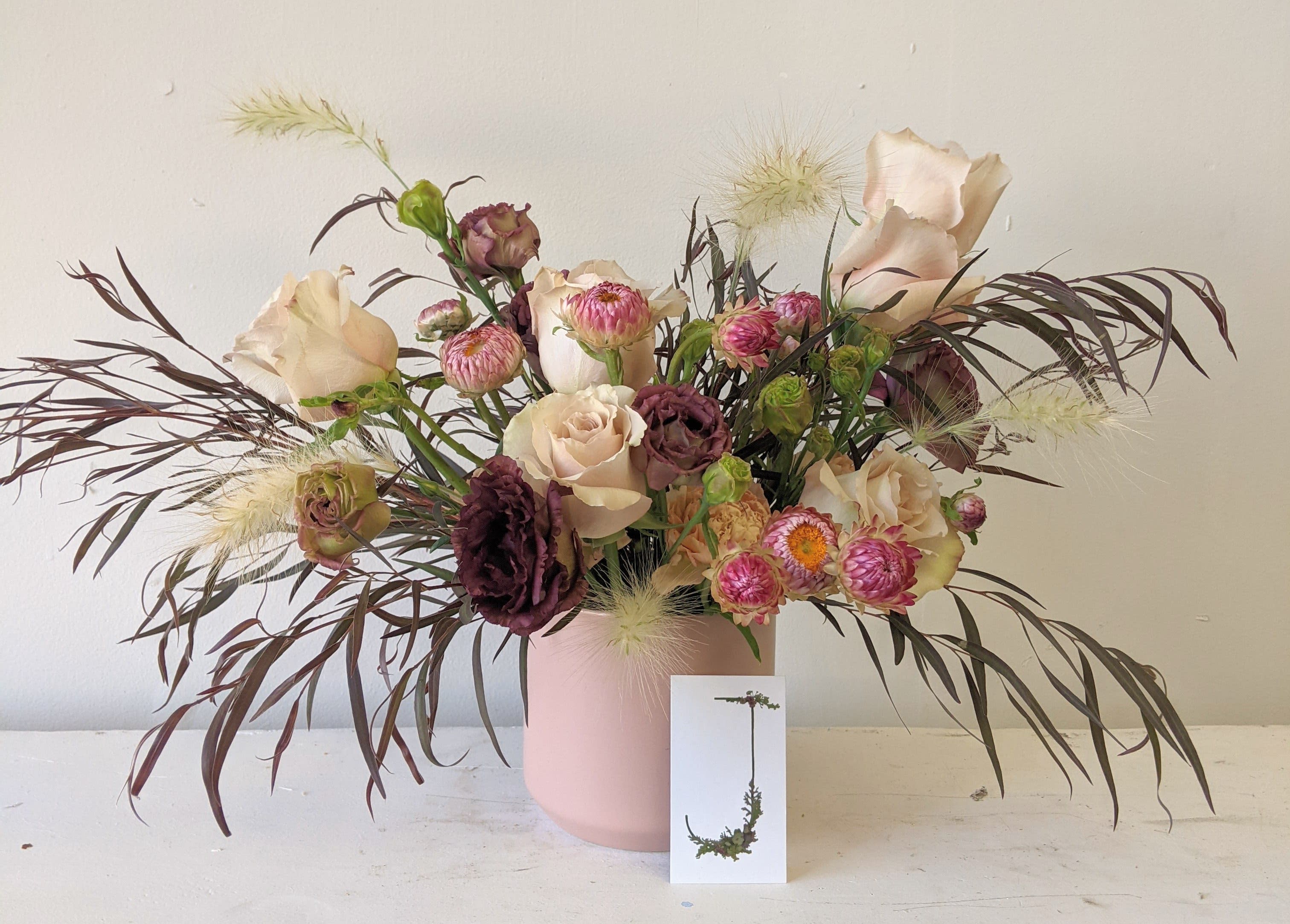 Mixed bouquet of blush and burgundy flowers in a pink vase