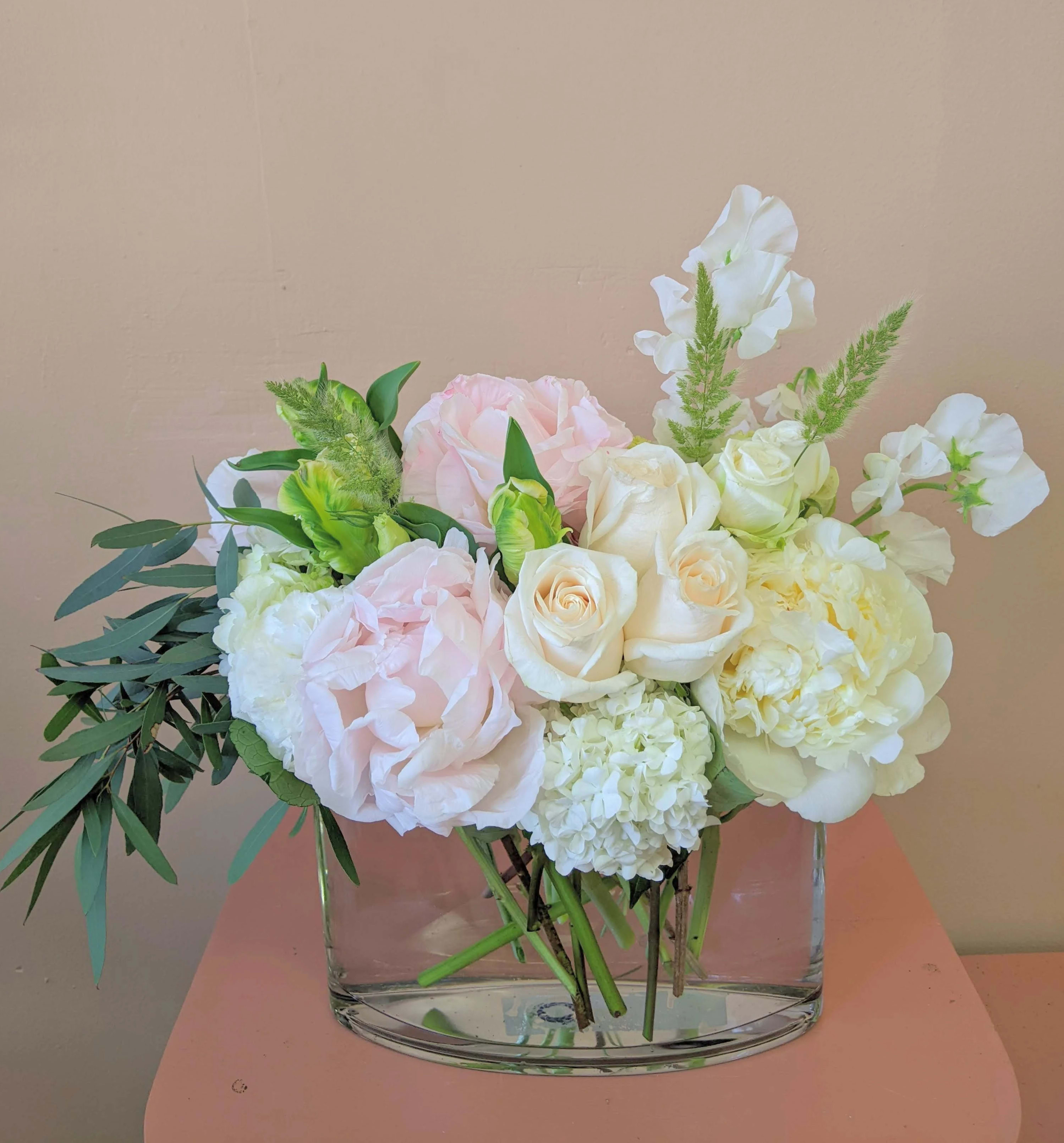 Pastel bouquet of roses, hydrangea, and white blooms in a clear glass vase